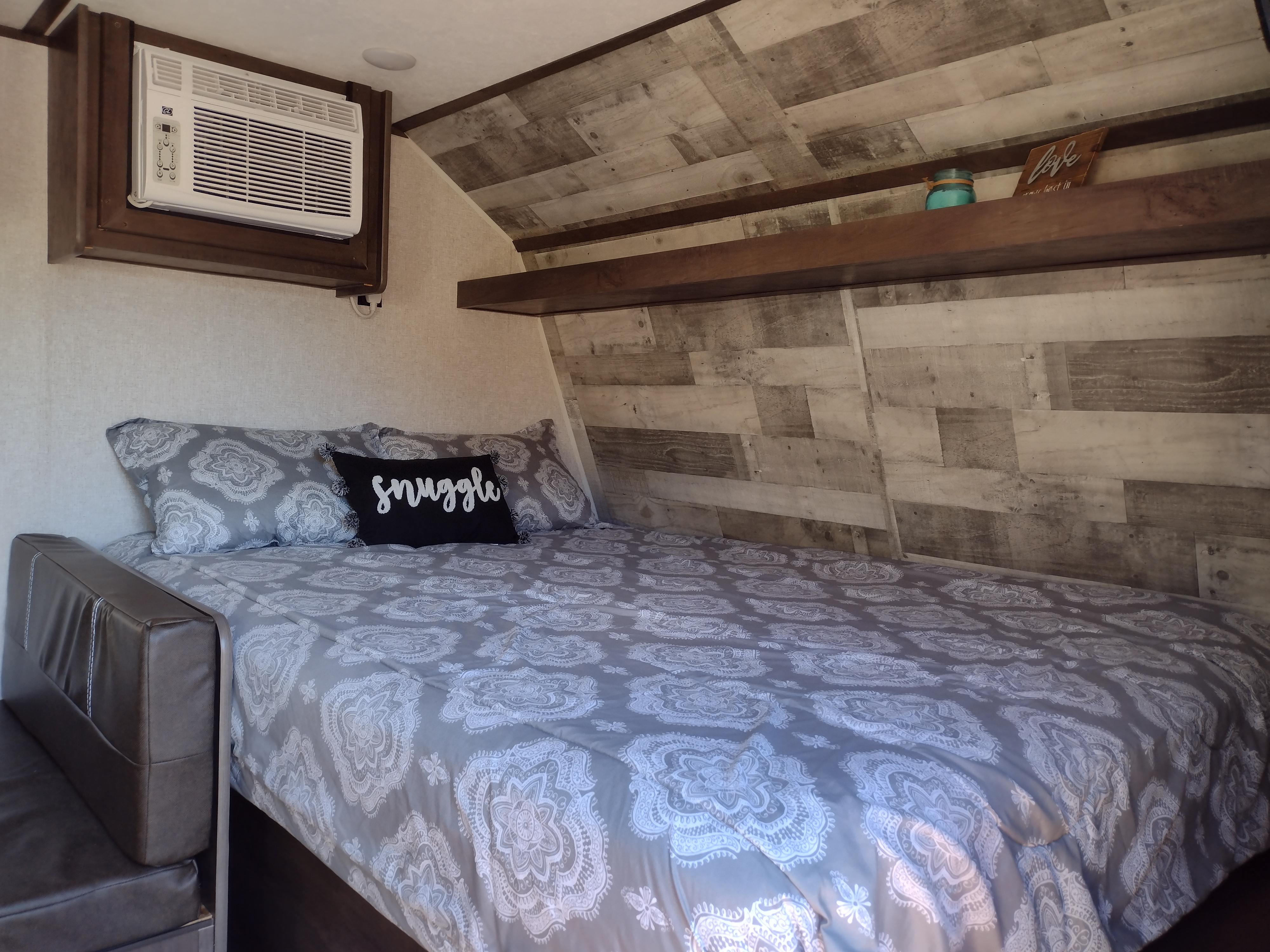 Inviting RV rental bedroom with a cozy bed, "snuggle" pillow, wall-mounted AC, and stylish wood-paneled walls for comfort.. Coleman Lantern 2022
