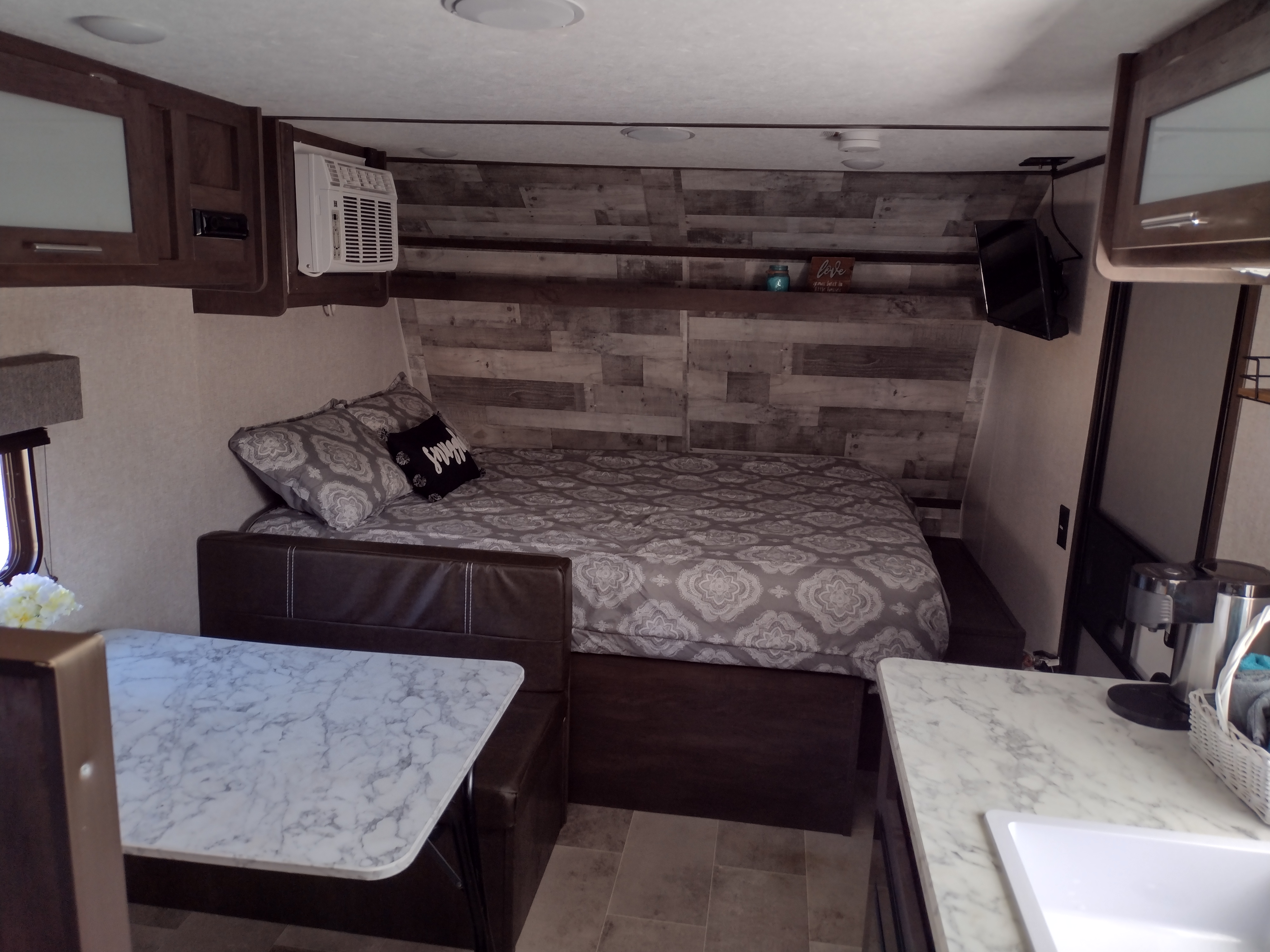 Cozy RV rental interior shows a patterned bed, marble dinette, small kitchen sink area, AC, and TV for comfort.. Coleman Lantern 2022