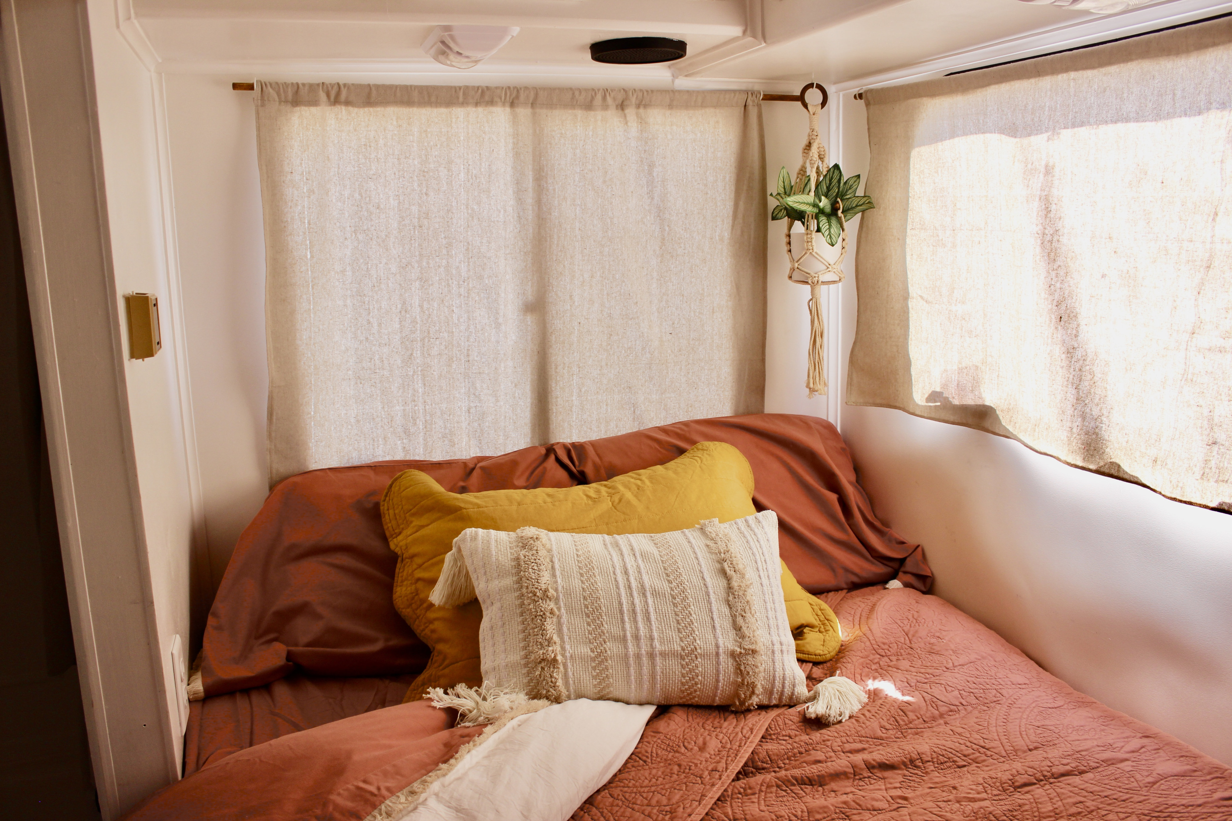 Cozy RV rental bedroom with warm-toned bedding, macrame plant, and natural light through linen curtains.. Gulf Stream Conquest 1995