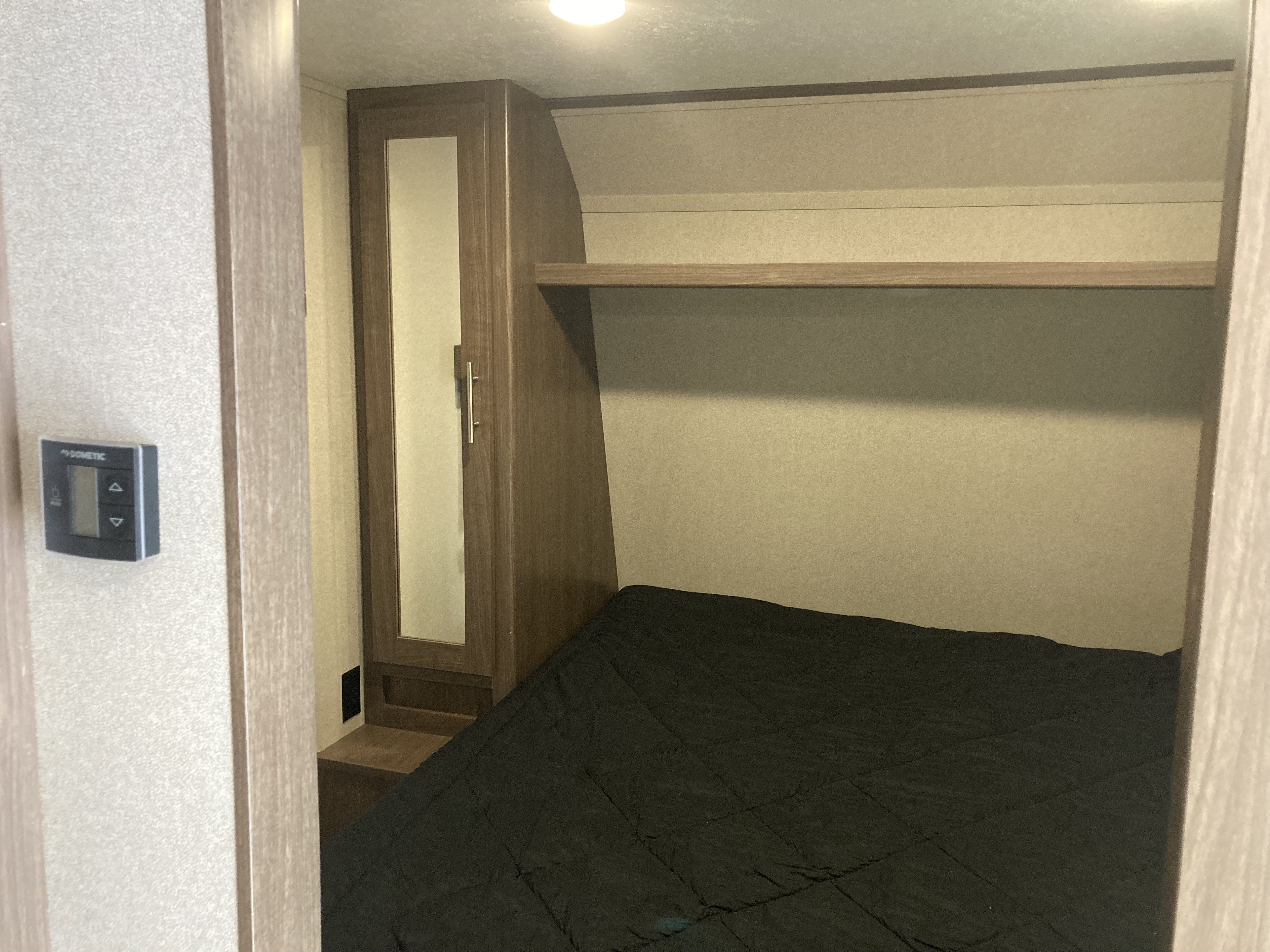 Inside an RV rental bedroom: a bed with black comforter, mirrored wardrobe, and Dometic thermostat on the wall.. Keystone Hideout 2019