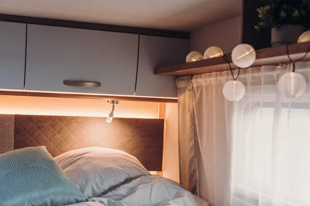 RV rental bedroom featuring a soft bed, warm ambient lighting, reading lamp, and decorative globe lights by the window.. Carado T459 2022