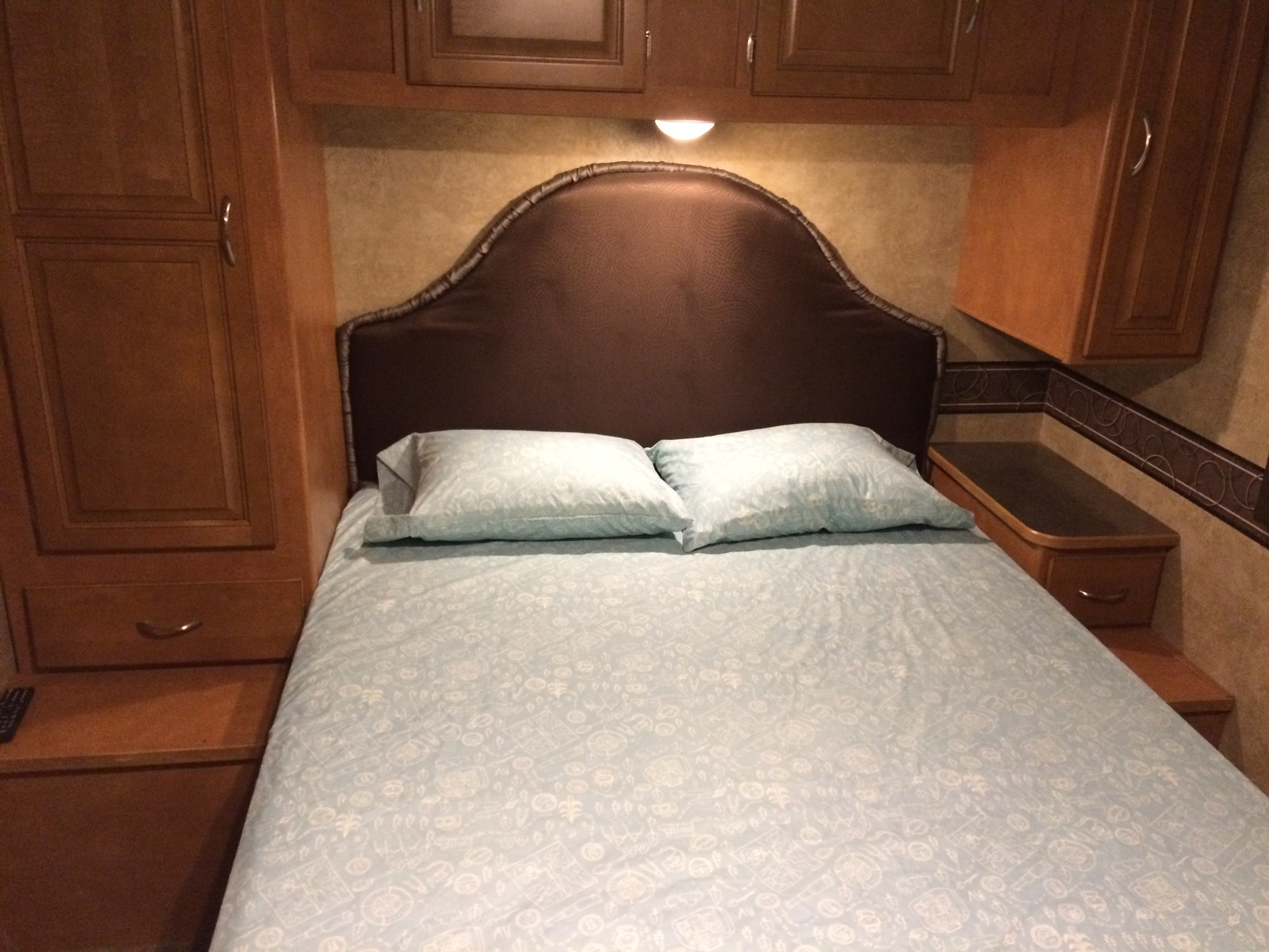 Comfortable RV rental bedroom with light blue patterned bedding, brown headboard, and built-in wood cabinetry.. Itasca Spirit 2014