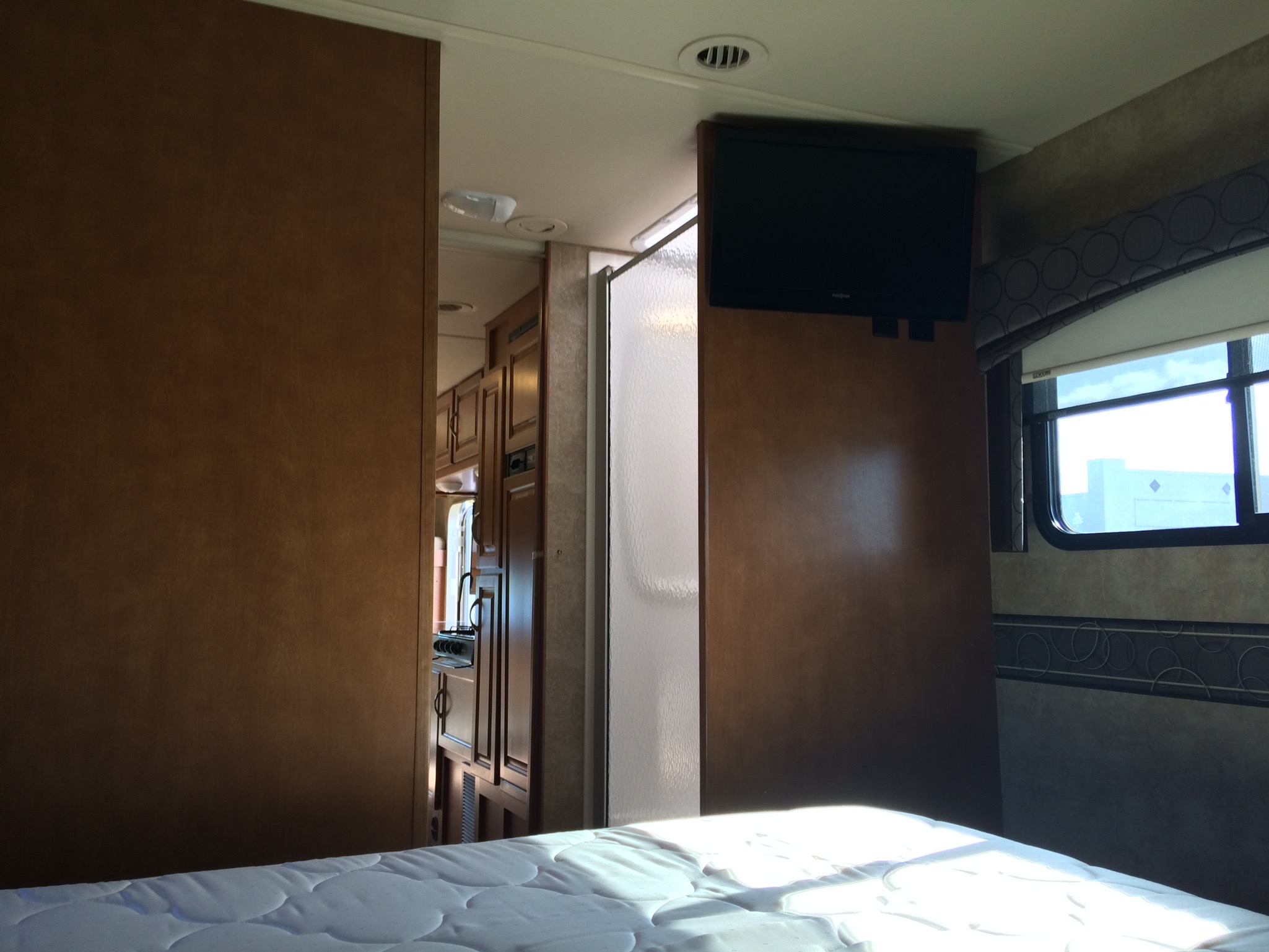Sunlit RV rental interior: A cozy bed, TV, and a glimpse of the kitchen/shower area. Experience mobile comfort.. Itasca Spirit 2014