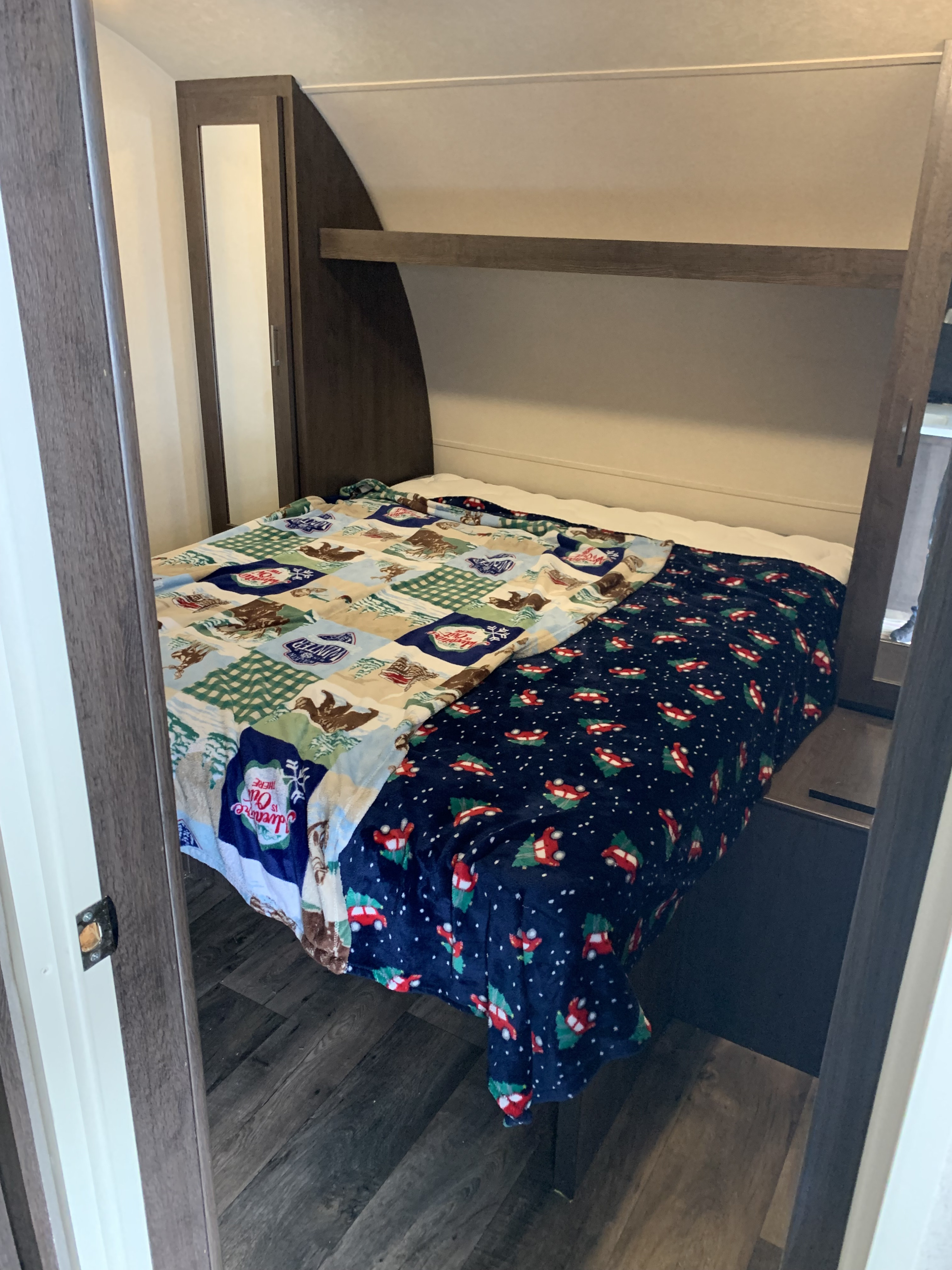 RV rental bedroom showcasing a compact bed with cozy, festive blankets and integrated storage overhead.. Forest River Wildwood 2018