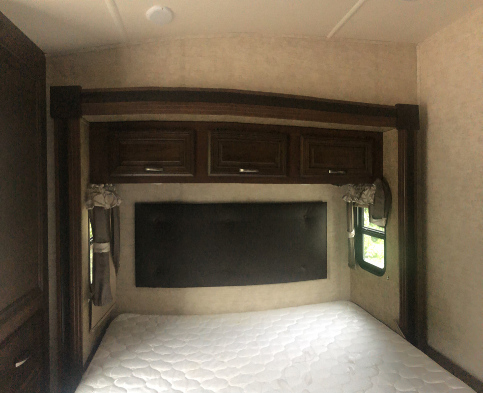 Clean RV rental bedroom featuring a white mattress, dark headboard, and overhead cabinets. Enjoy compact comfort.. Forest River Sierra 2017