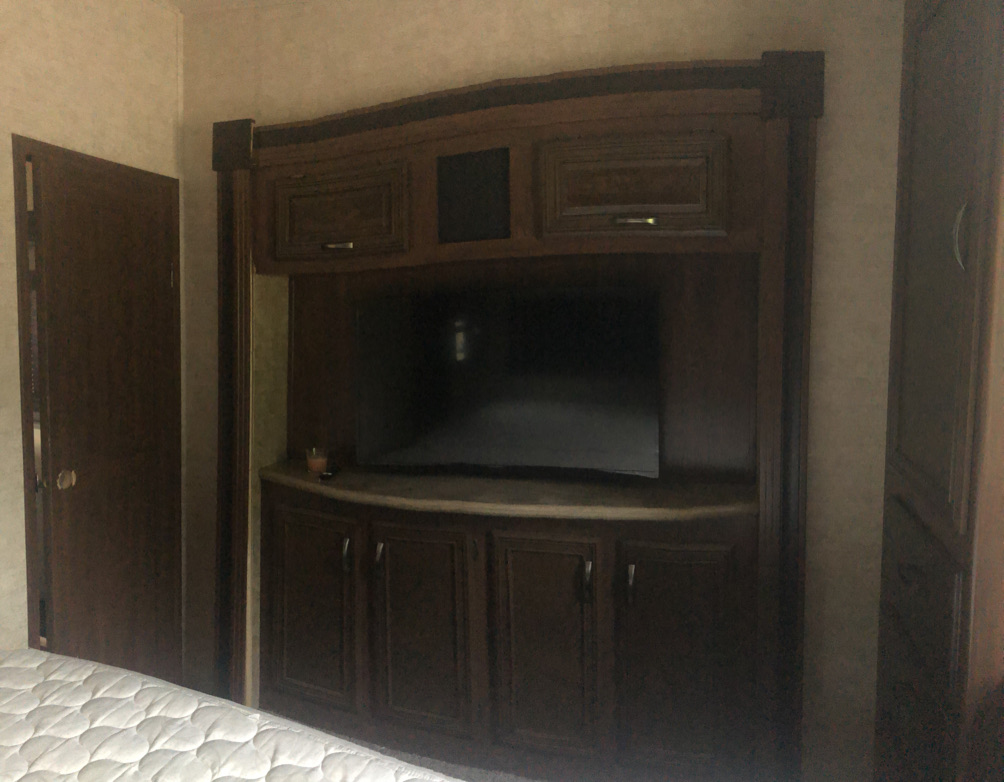 Cozy RV rental bedroom featuring a built-in entertainment unit with TV, wood cabinetry, and a door on the left.. Forest River Sierra 2017
