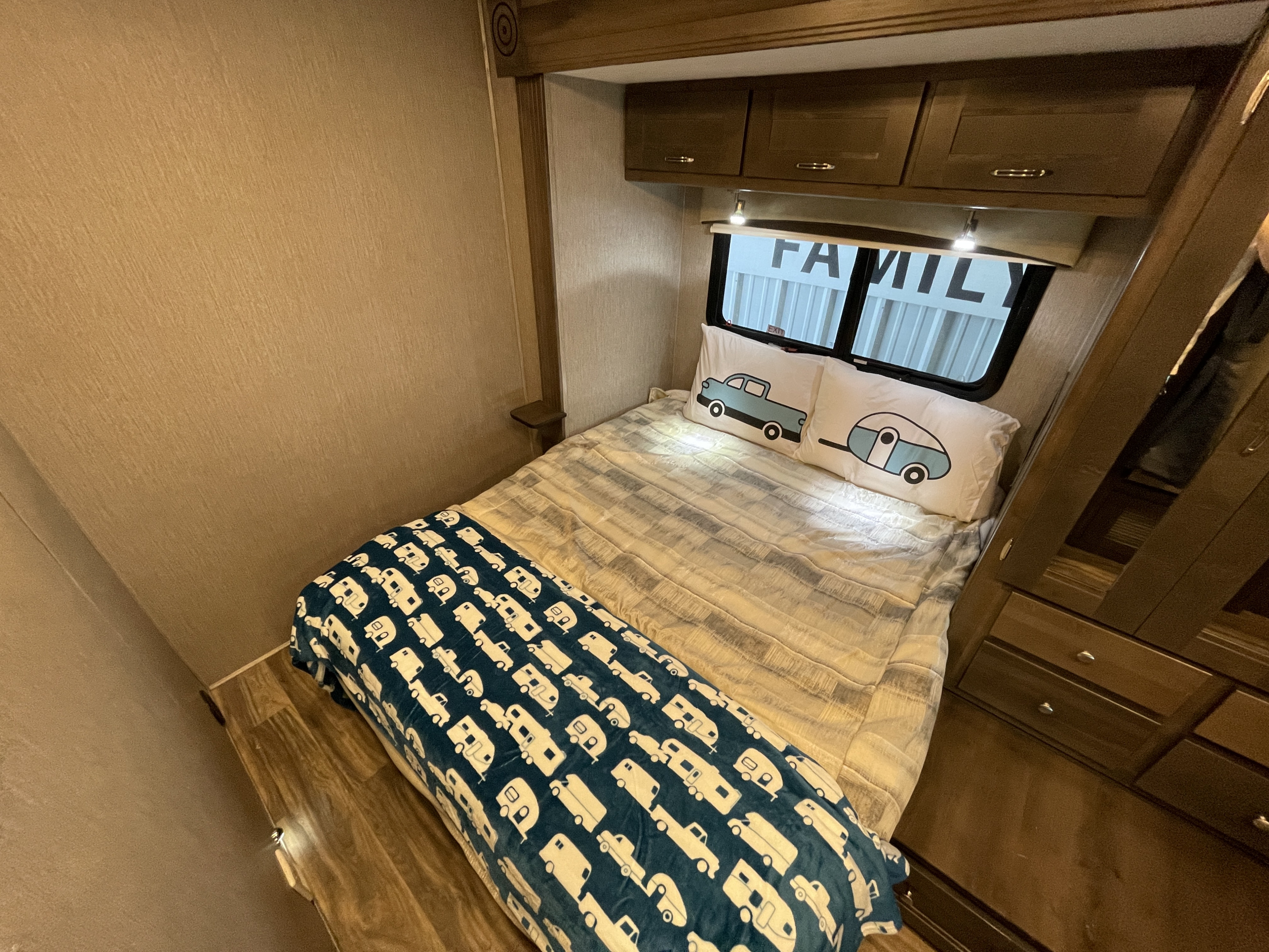 This cozy RV rental bedroom features a comfy bed with unique truck/camper pillows and an RV-themed blanket, plus useful overhead storage.. Nexus Triumph 2021