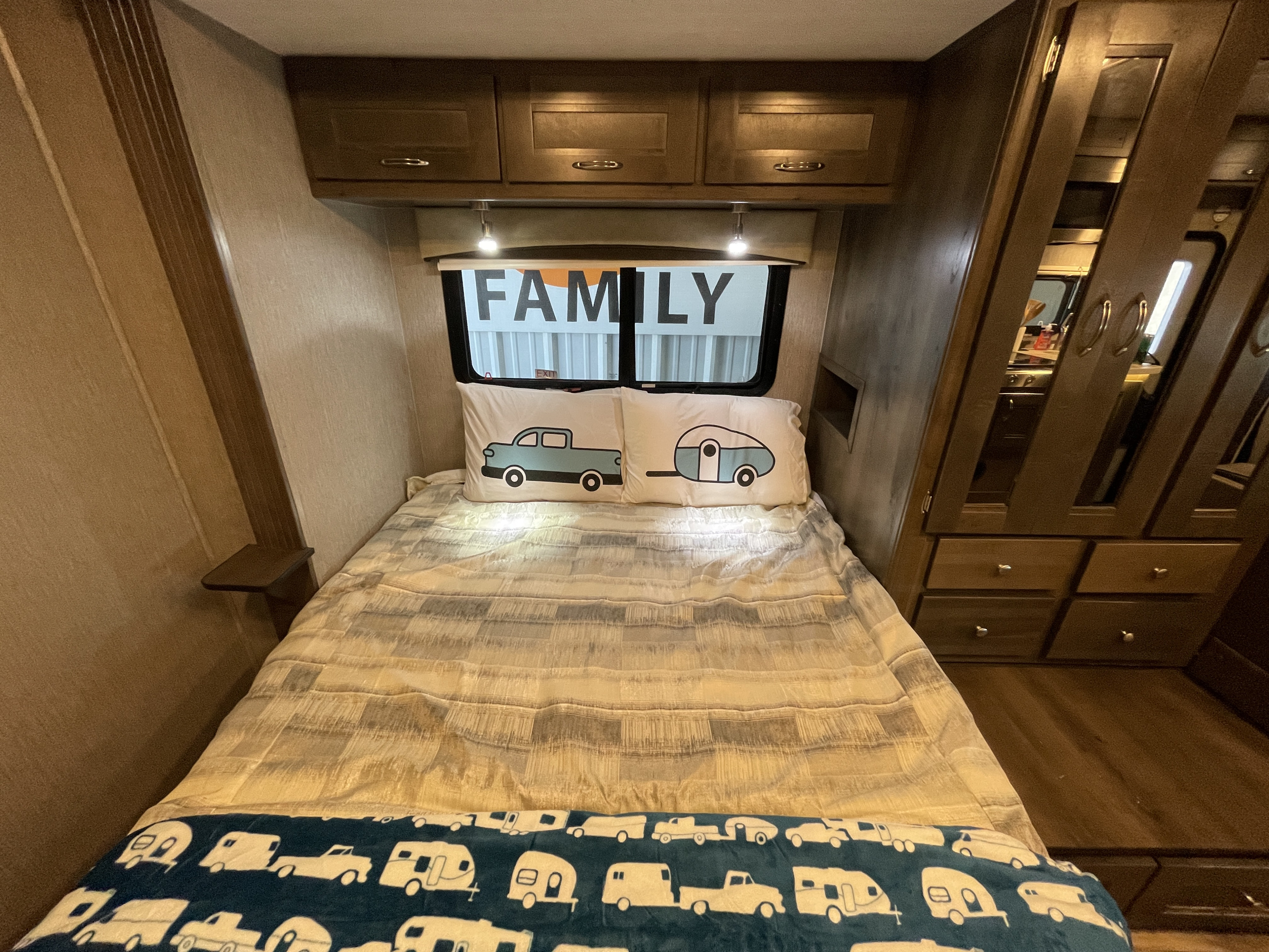Cozy RV rental family bedroom: inviting bed with truck/camper pillows, overhead cabinets, and ample built-in storage.. Nexus Triumph 2021
