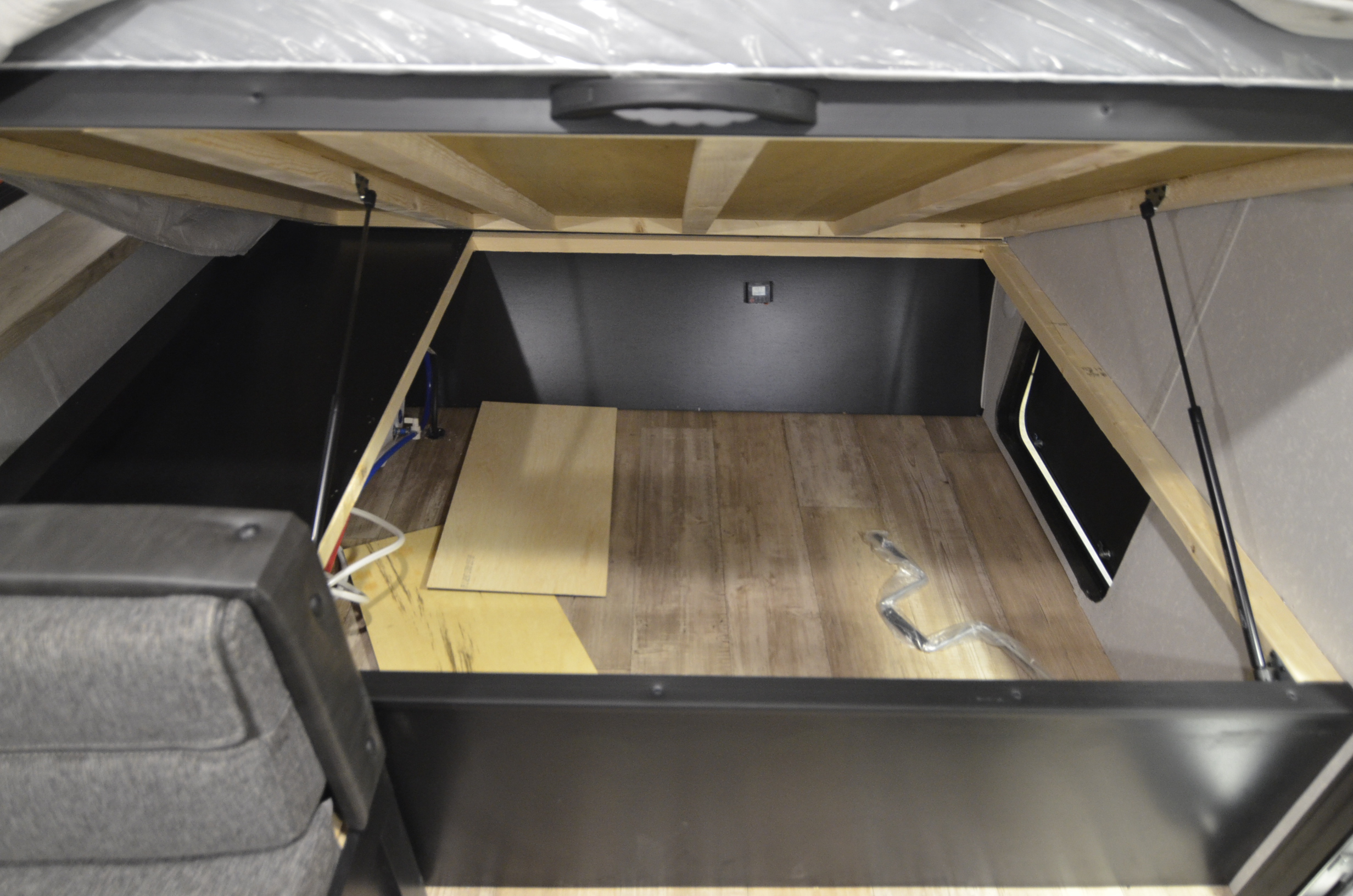 View of ample under-bed storage in an RV rental. Lifted mattress reveals a large, tidy compartment with wooden floor.. Forest River Cherokee 2021