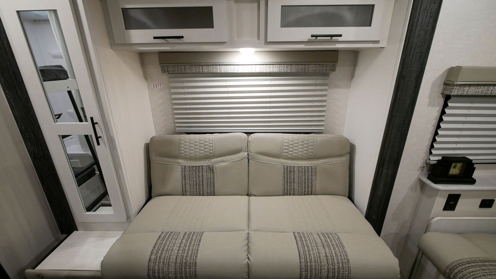 Modern RV rental interior showing a sofa/bed, overhead storage, window, and glimpsed bunk beds through the door.. Forest River R-Pod 2022