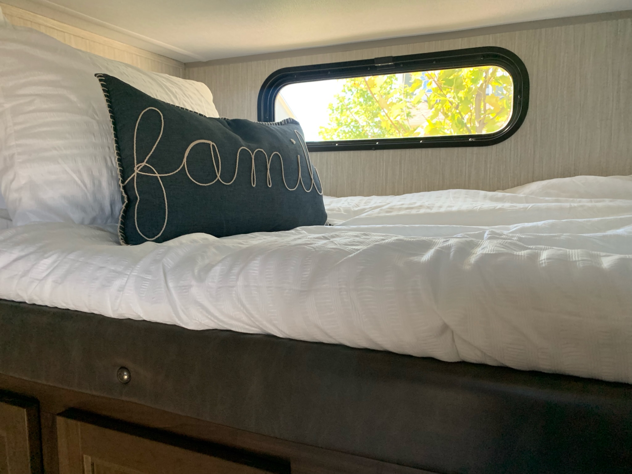 Cozy RV rental bed featuring a "family" embroidered pillow and natural light from the window.. Forest River Cherokee Grey Wolf 2021