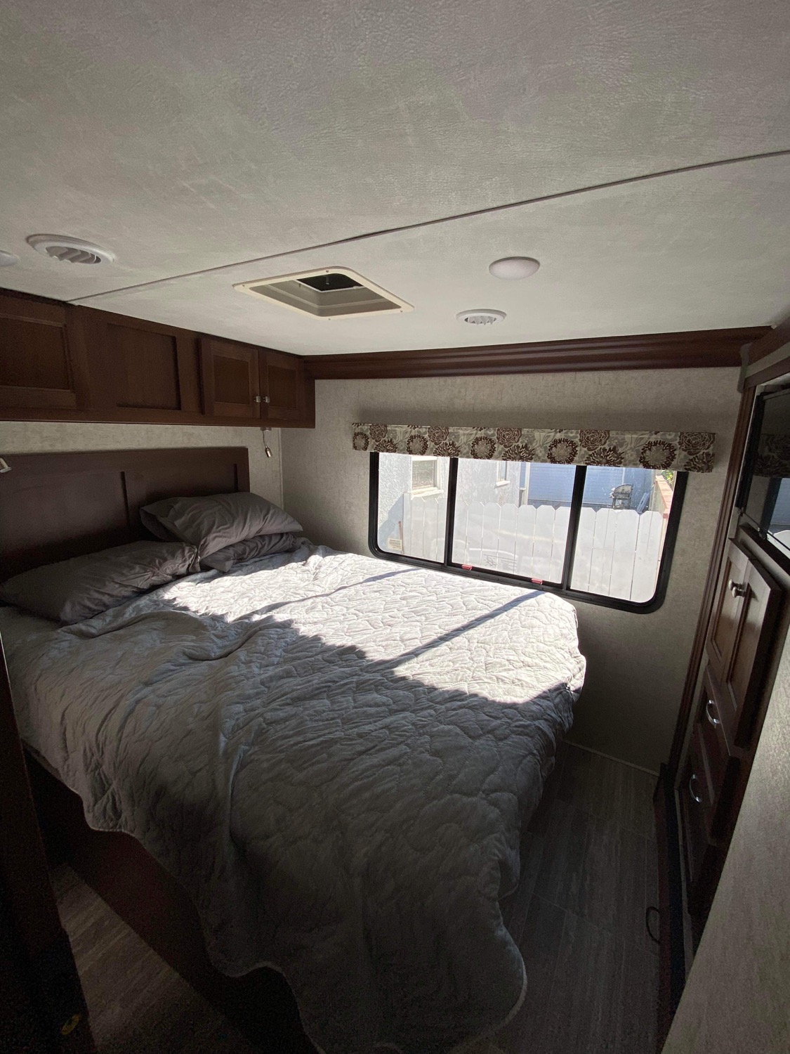 Bright RV rental bedroom showing a large bed with grey bedding, wood cabinets, and window with natural light.. Forest River Forester 2019