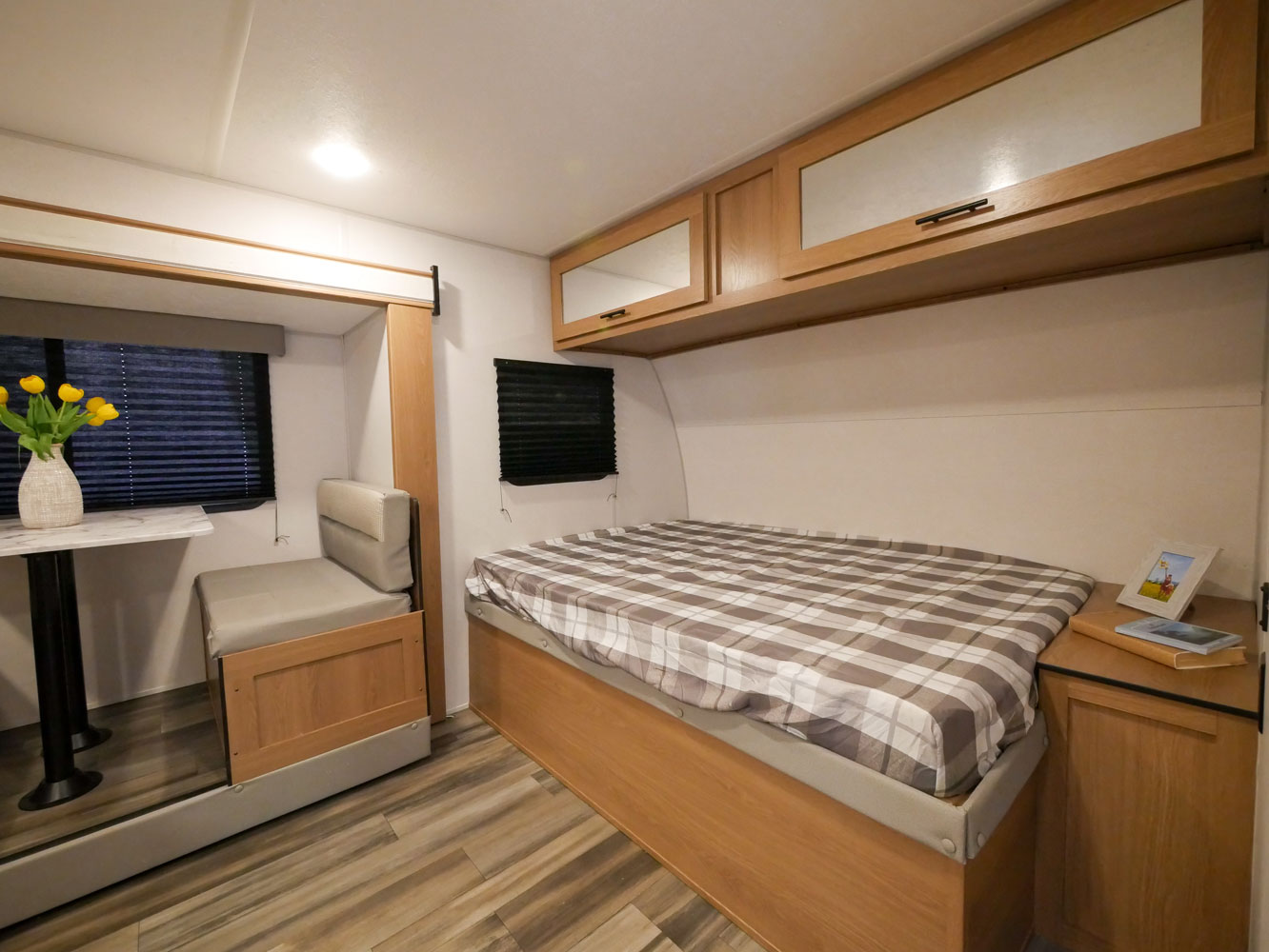 RV rental interior showing a compact bedroom with a plaid bed and an adjacent dinette for dining/seating.. Prime Time Avenger 2022