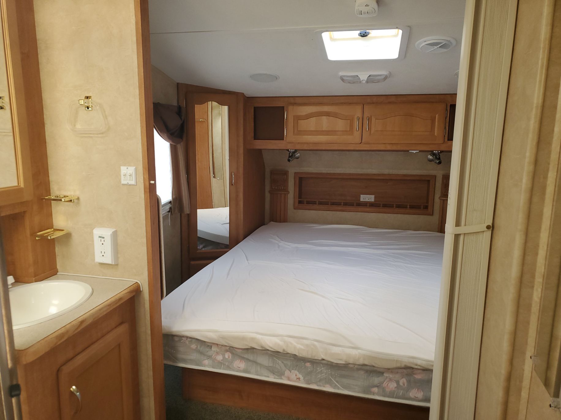 RV rental interior: A cozy bedroom with a white-sheeted bed, adjacent to a compact bathroom vanity. Ideal for adventures.. Forest River Wildcat 2008