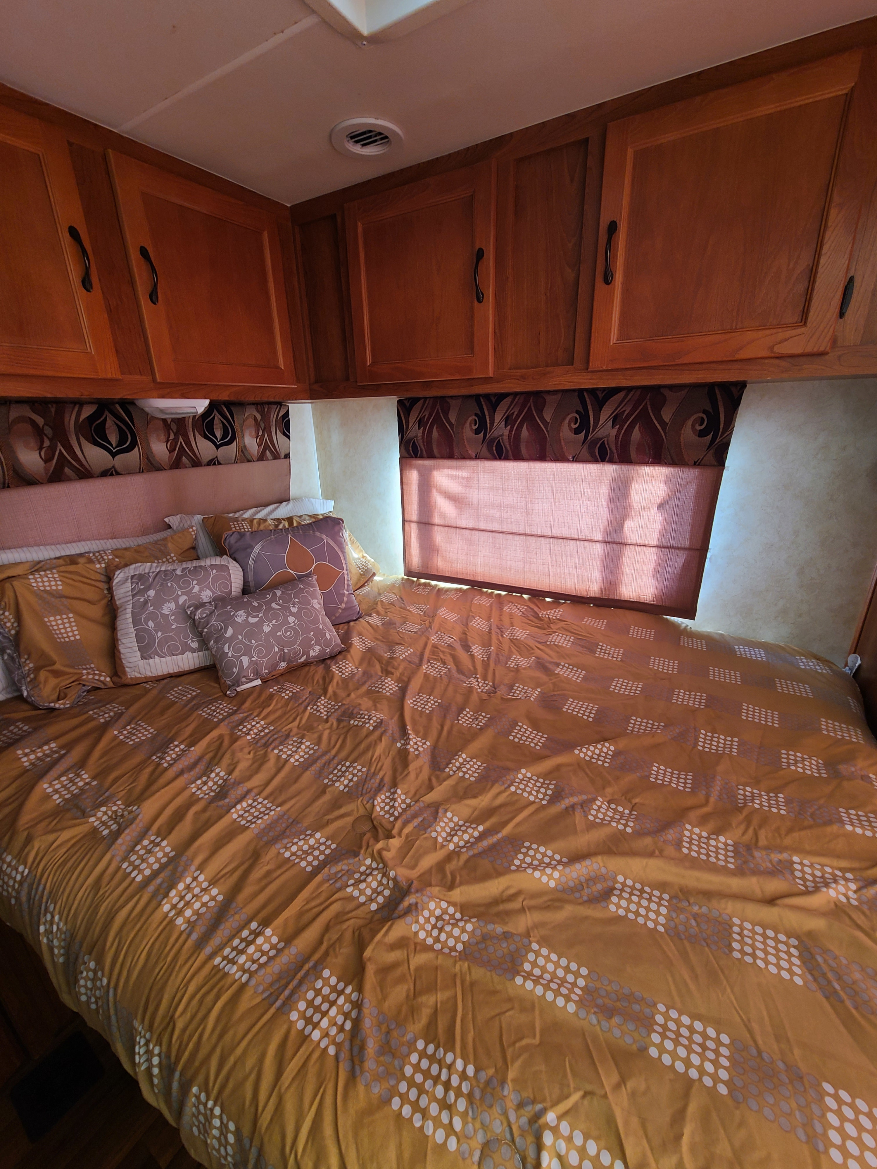 Cozy RV rental bedroom with patterned bedding, overhead cabinets, and a window, perfect for comfortable travel.. Coachmen Freelander 2011