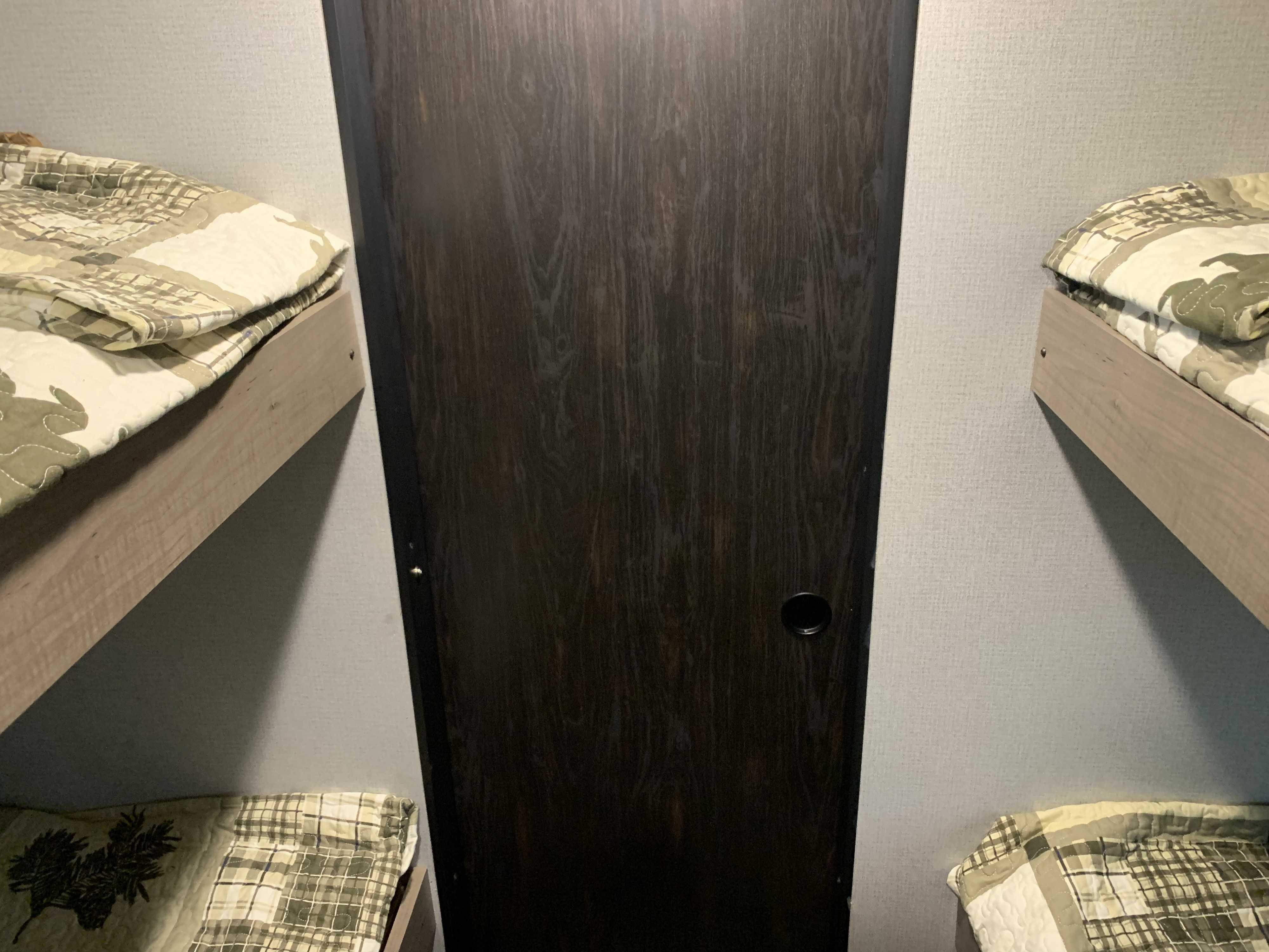 Inside an **RV rental**: cozy bunk beds with quilted blankets flanking a dark wood cabinet/door.. Keystone Hideout 2020