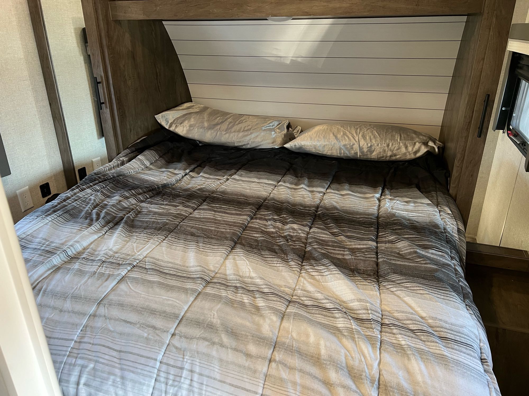 This inviting RV rental bedroom offers a comfortable bed with a striped grey and white comforter & pillows.. Forest River Wildwood X-Lite 2021