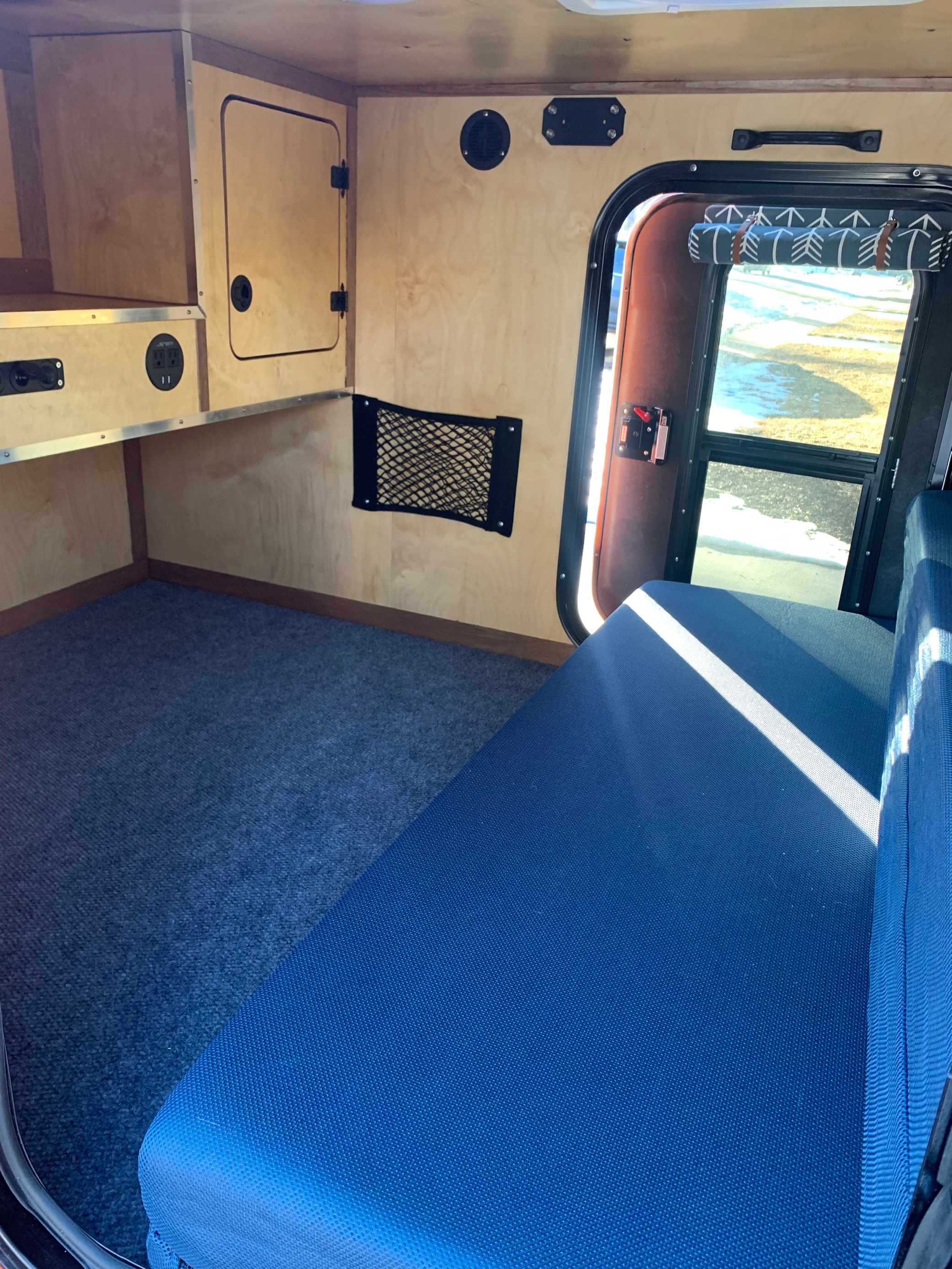 Compact RV rental interior: wood-paneled walls, built-in storage, power outlets, blue carpet, and a comfortable sleeping area.. Vintage Trailer Works XTR 2021