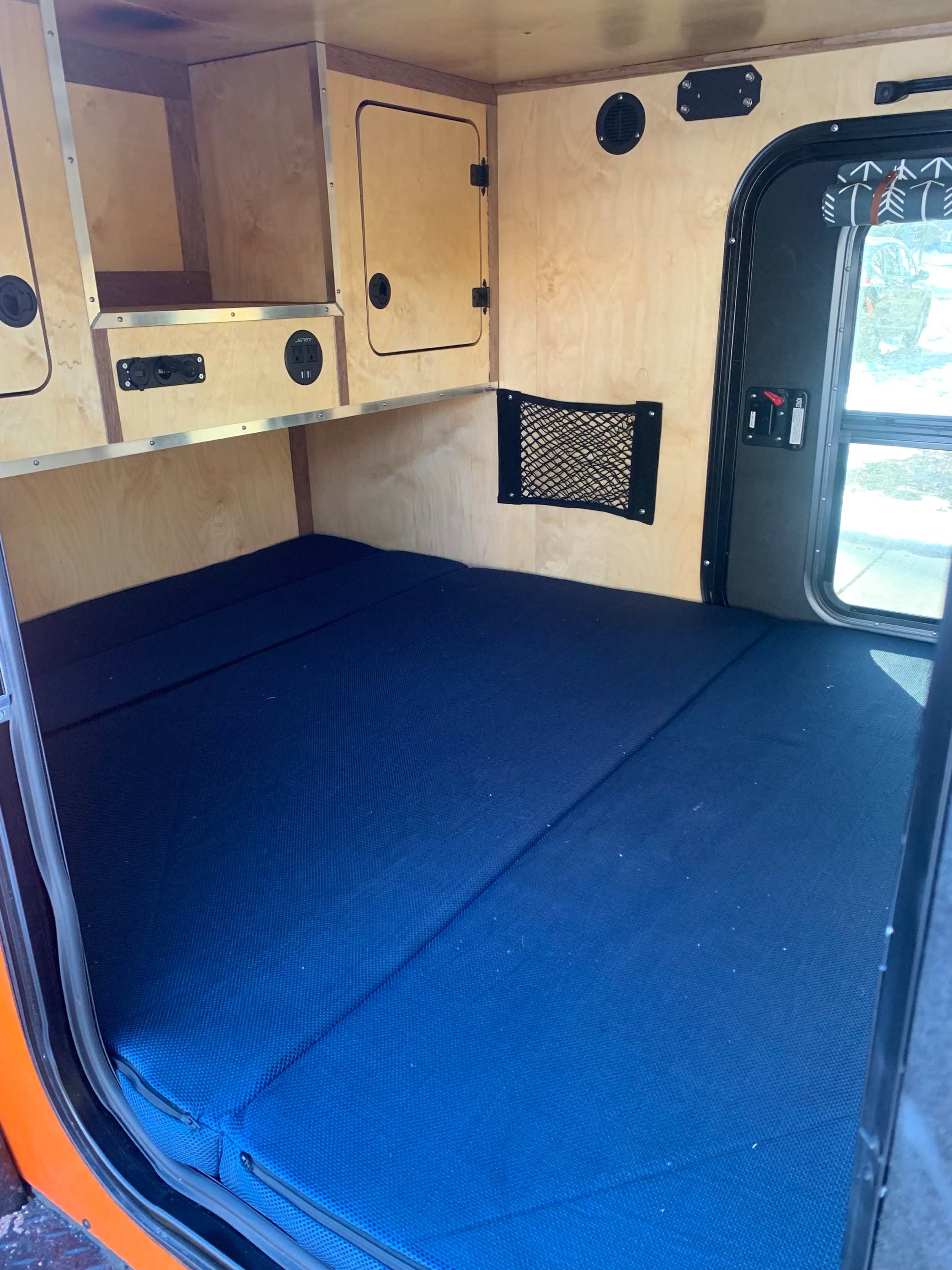 Cozy rv rental interior featuring a blue mattress, wood storage, and power outlets. Compact and functional sleeping area.. Vintage Trailer Works XTR 2021