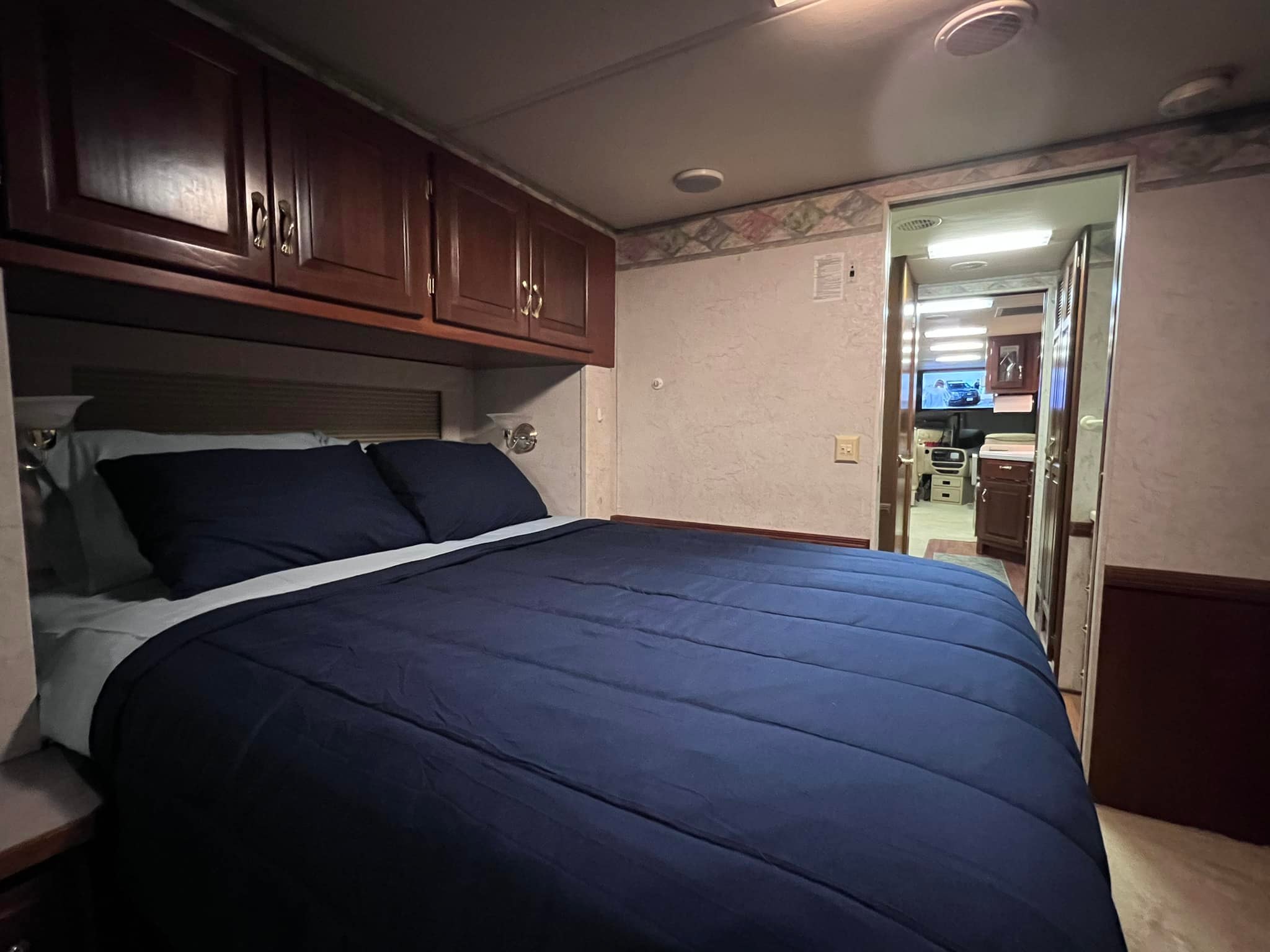 Cozy RV rental bedroom featuring a large bed with blue bedding, overhead cabinets, and a hallway view. Ideal for travel.. Dutch Star Dutch Star Motorhome 2002