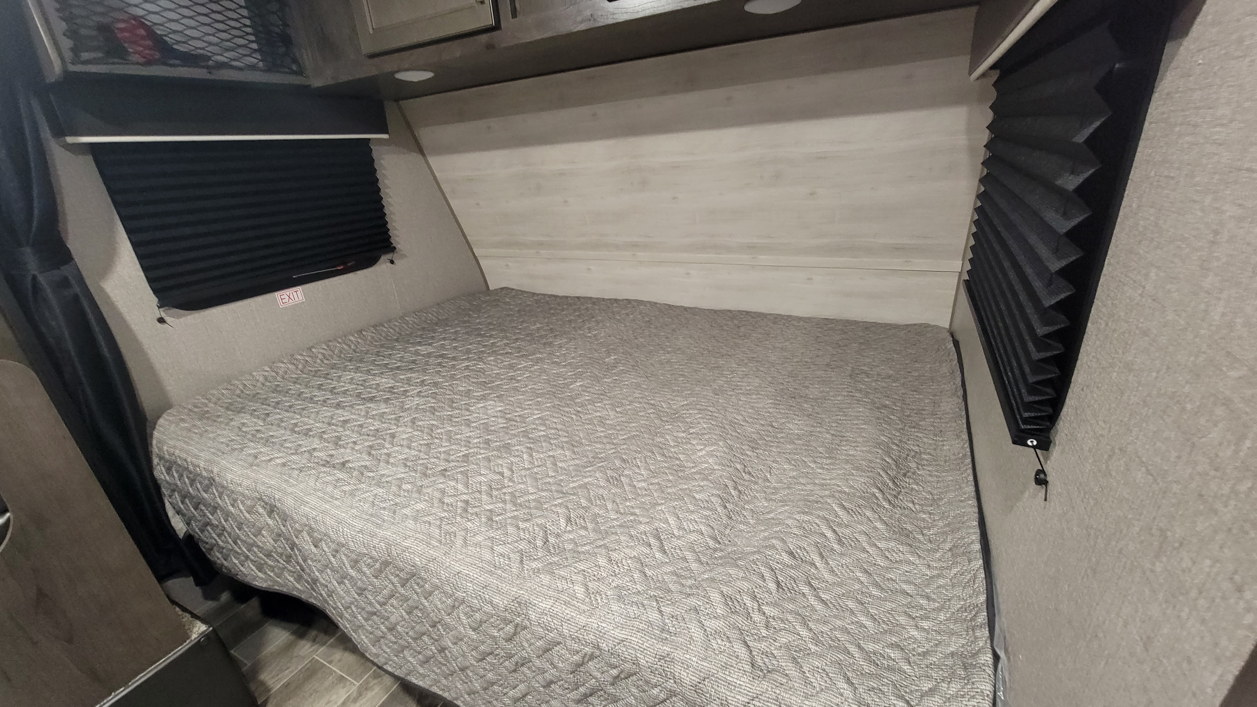 RV rental bedroom: a bed with a gray textured quilt, light wood walls, black pleated blinds, and overhead storage for travelers.. Jayco Jay Flight 184bhs 2021