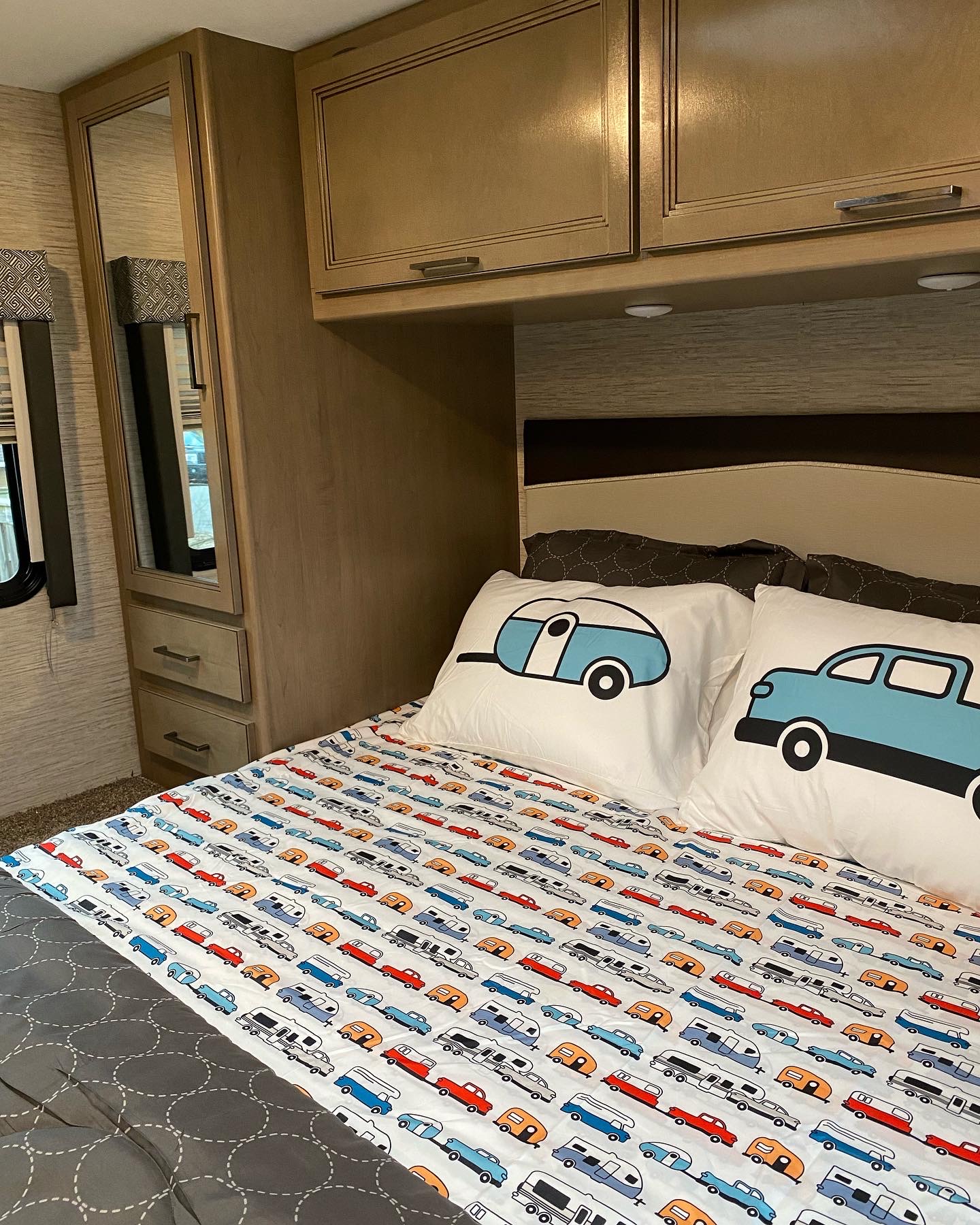 Cozy RV rental bedroom with travel-themed bedding, featuring a mirrored wardrobe, overhead cabinets, and a window.. Thor Magnitude 2022