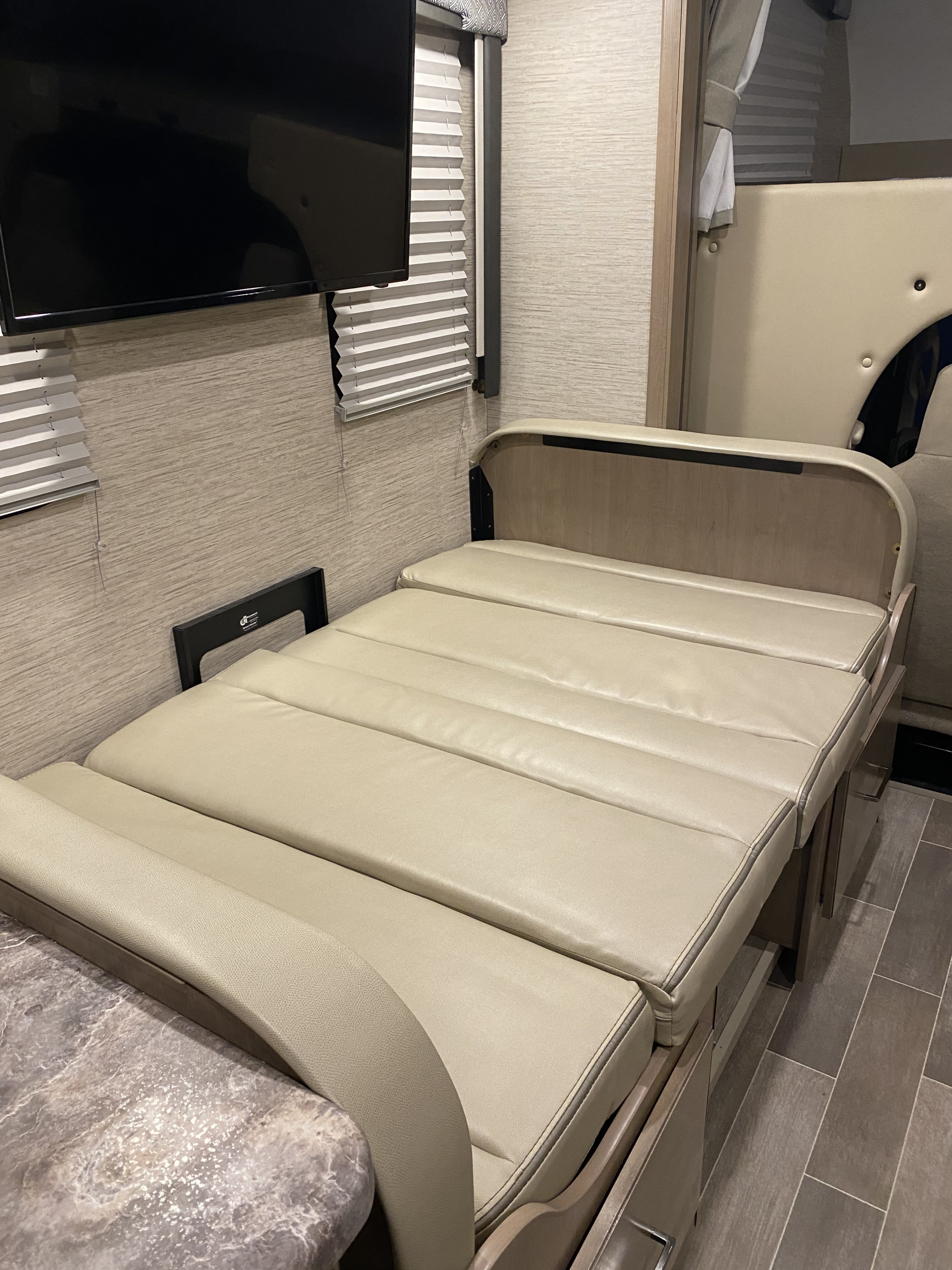 Inside an RV rental: a beige dinette folded down into a bed, with a TV overhead & tiled floor.. Thor Magnitude 2022