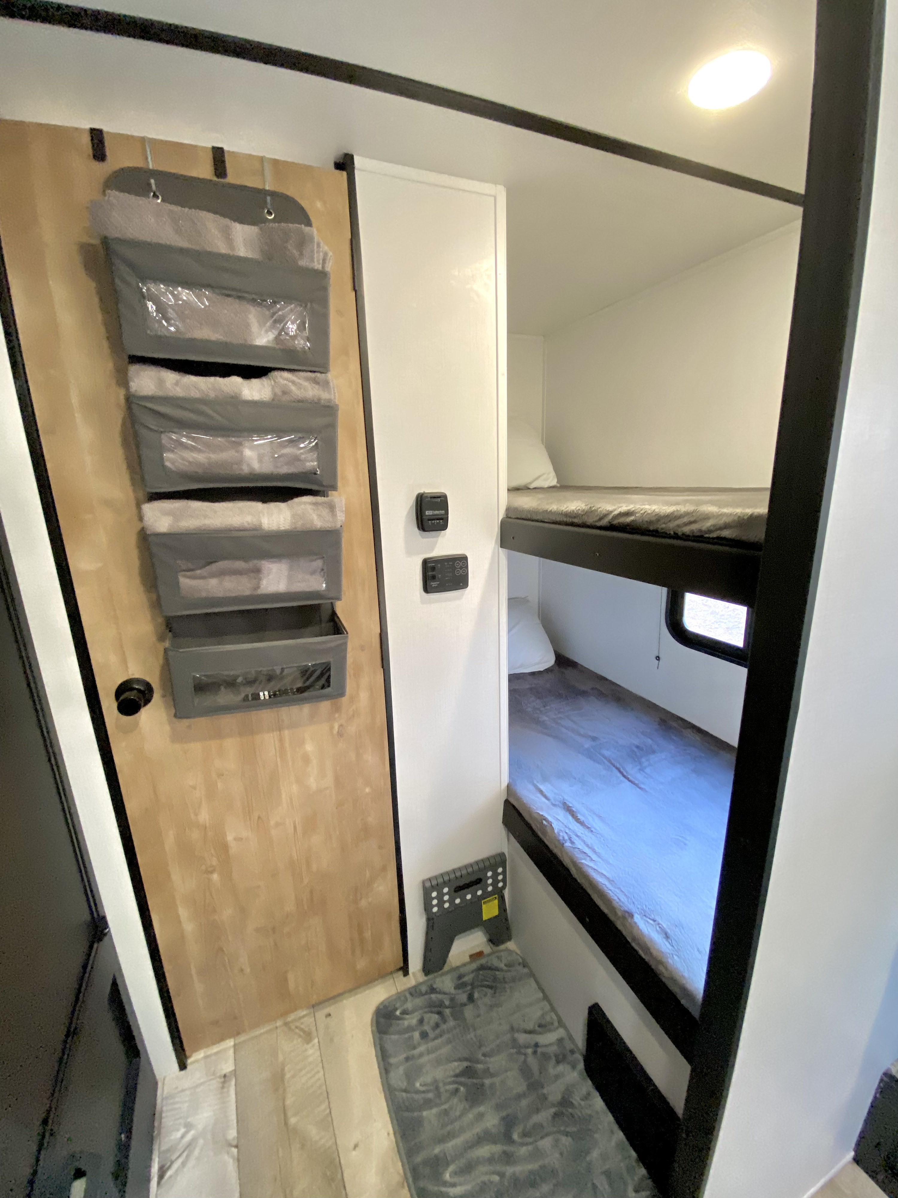 Inside an RV rental, showing compact bunk beds with a soft grey rug and a door-mounted storage organizer.. Keystone Springdale 2022