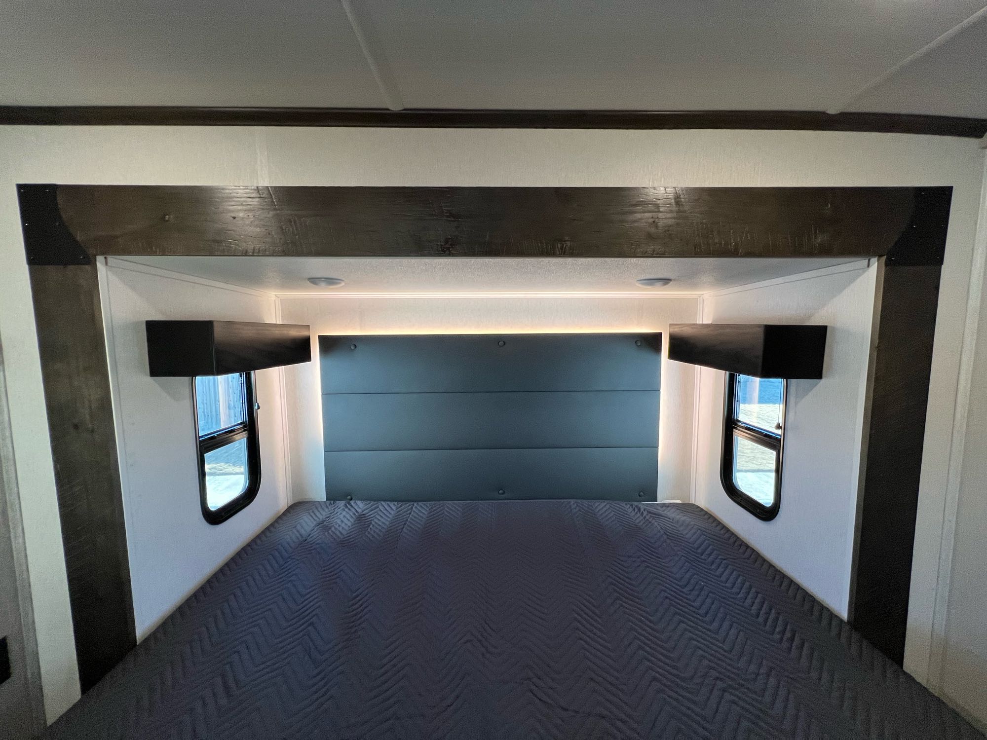 Experience comfort in this RV rental's modern bedroom, featuring a large bed with a padded headboard, windows, and accent lighting.. Forest River Cardinal 2022