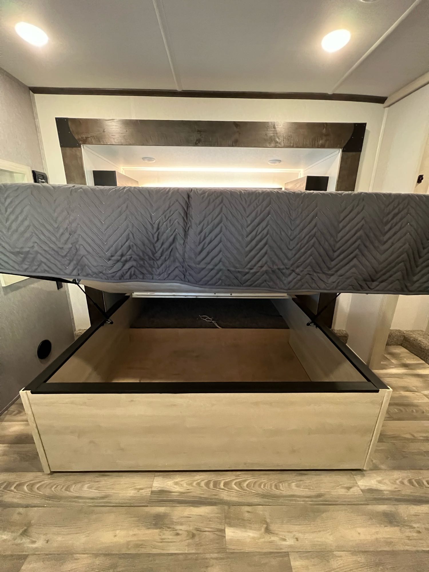 RV rental bed with under-bed storage lifted, featuring a grey quilted mattress in a spacious RV interior.. Forest River Cardinal 2022