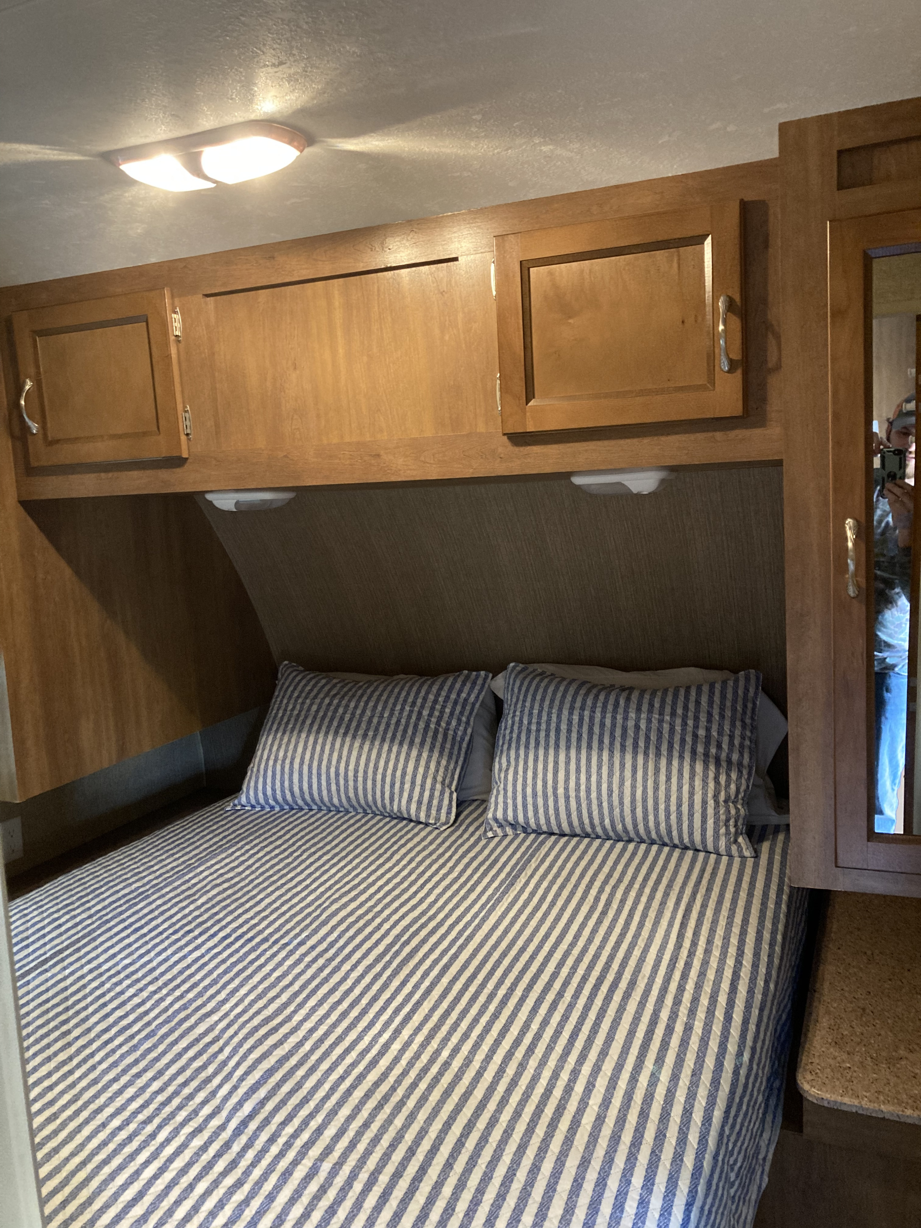 RV rental bedroom with striped bedding, overhead cabinets, bright lighting, and a mirror reflecting the interior space.. Coachmen Catalina 2015