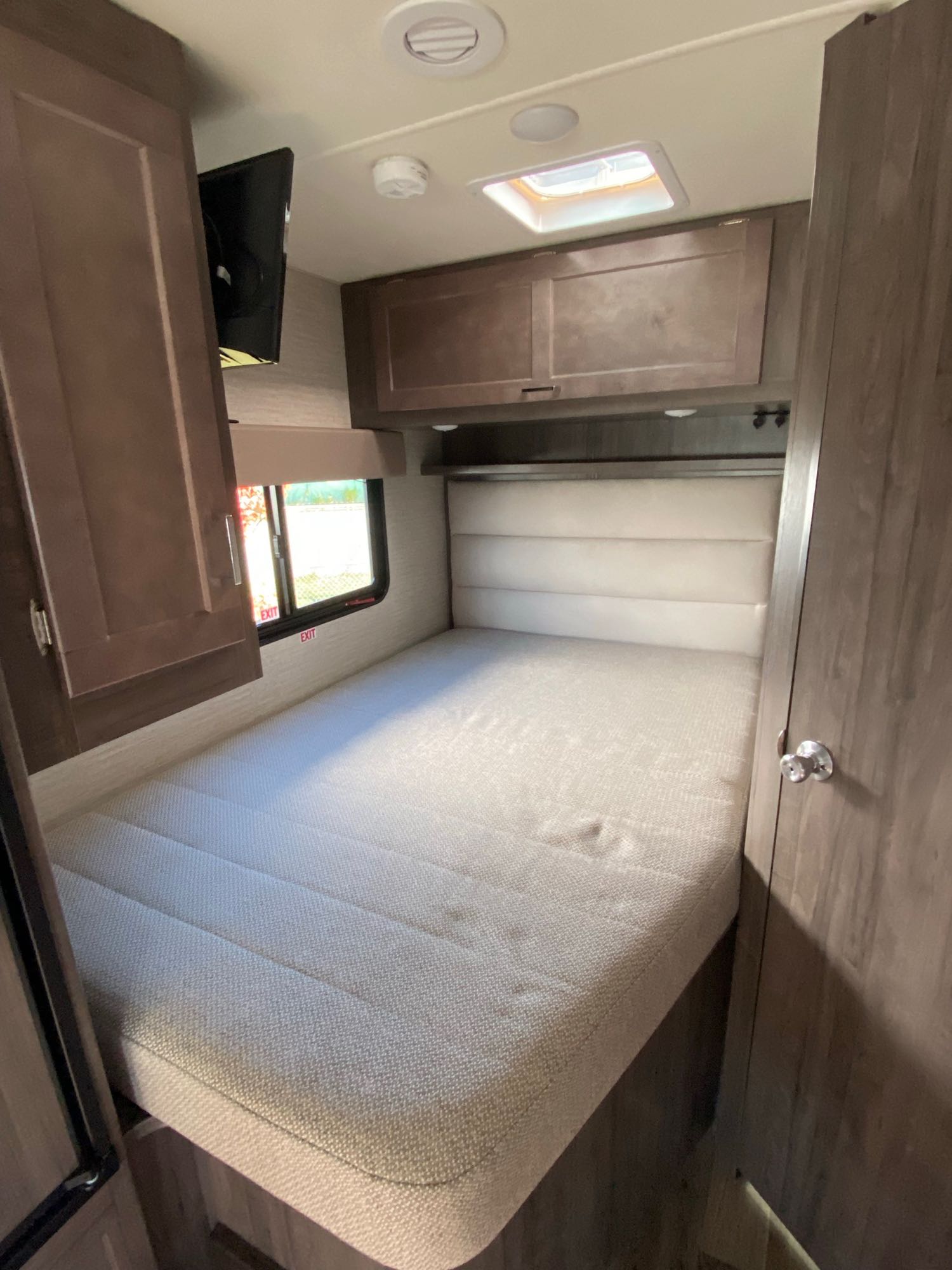 This inviting RV rental bedroom features a comfy mattress, upholstered headboard, overhead cabinets, TV, and window.. Winnebago Minnie Winnie 2022