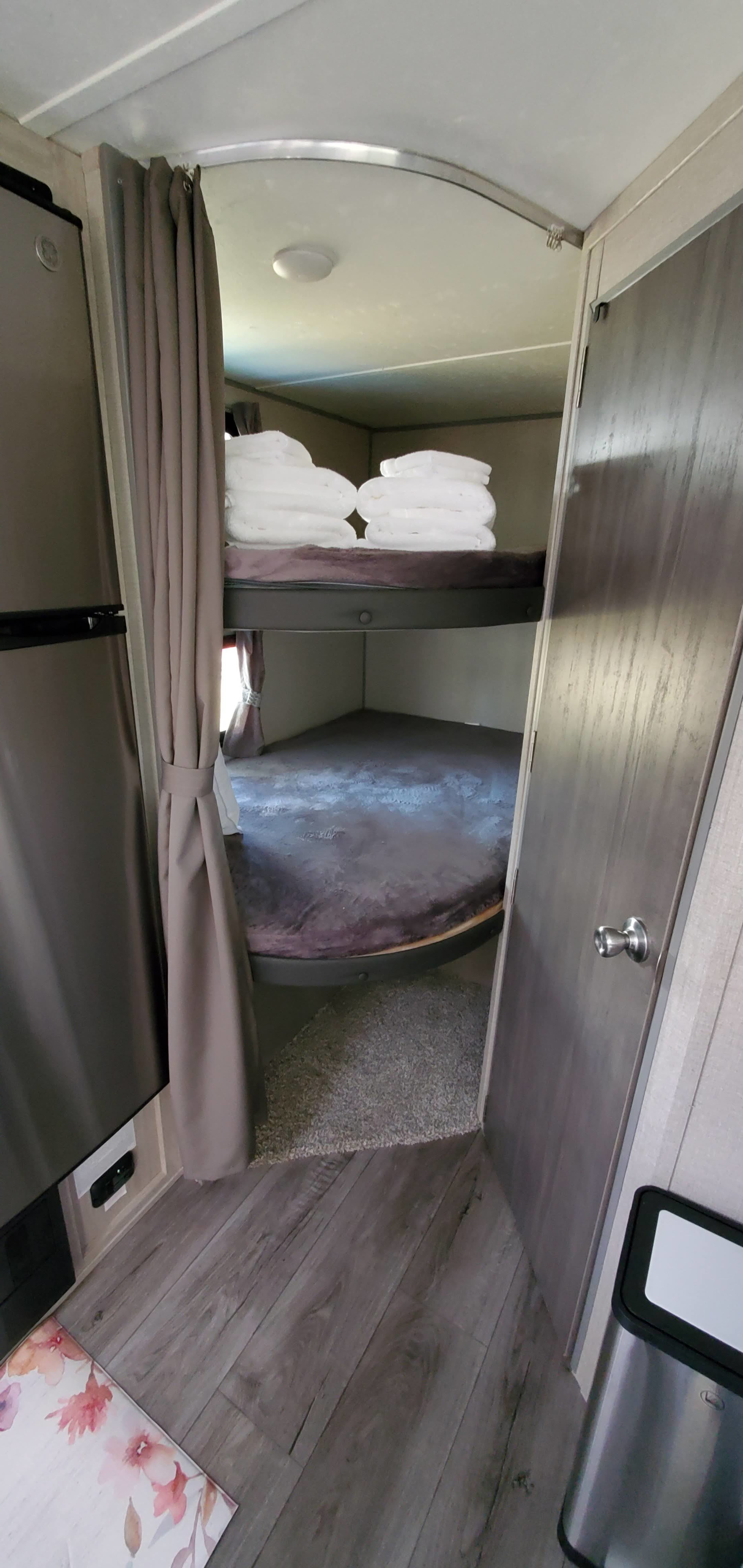 An RV rental's bunk bed area, featuring a stacked bed with white towels, a bottom bunk, and a fridge nearby.. Forest River Coachmen Catalina 184BHS 2022