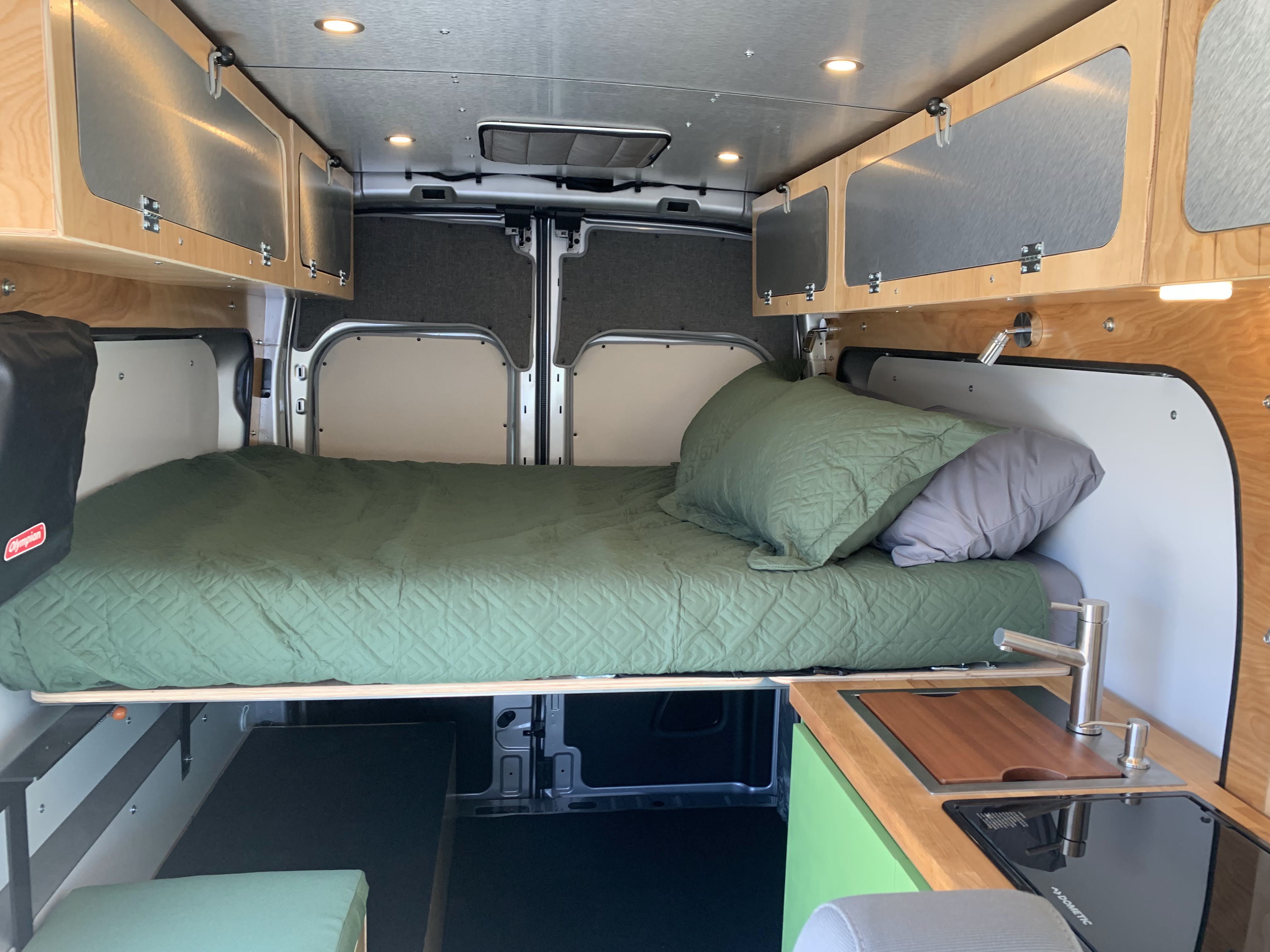 Cozy RV rental interior with a comfortable bed, compact kitchen, and overhead cabinets for storage.. Ford Transit 250 2021