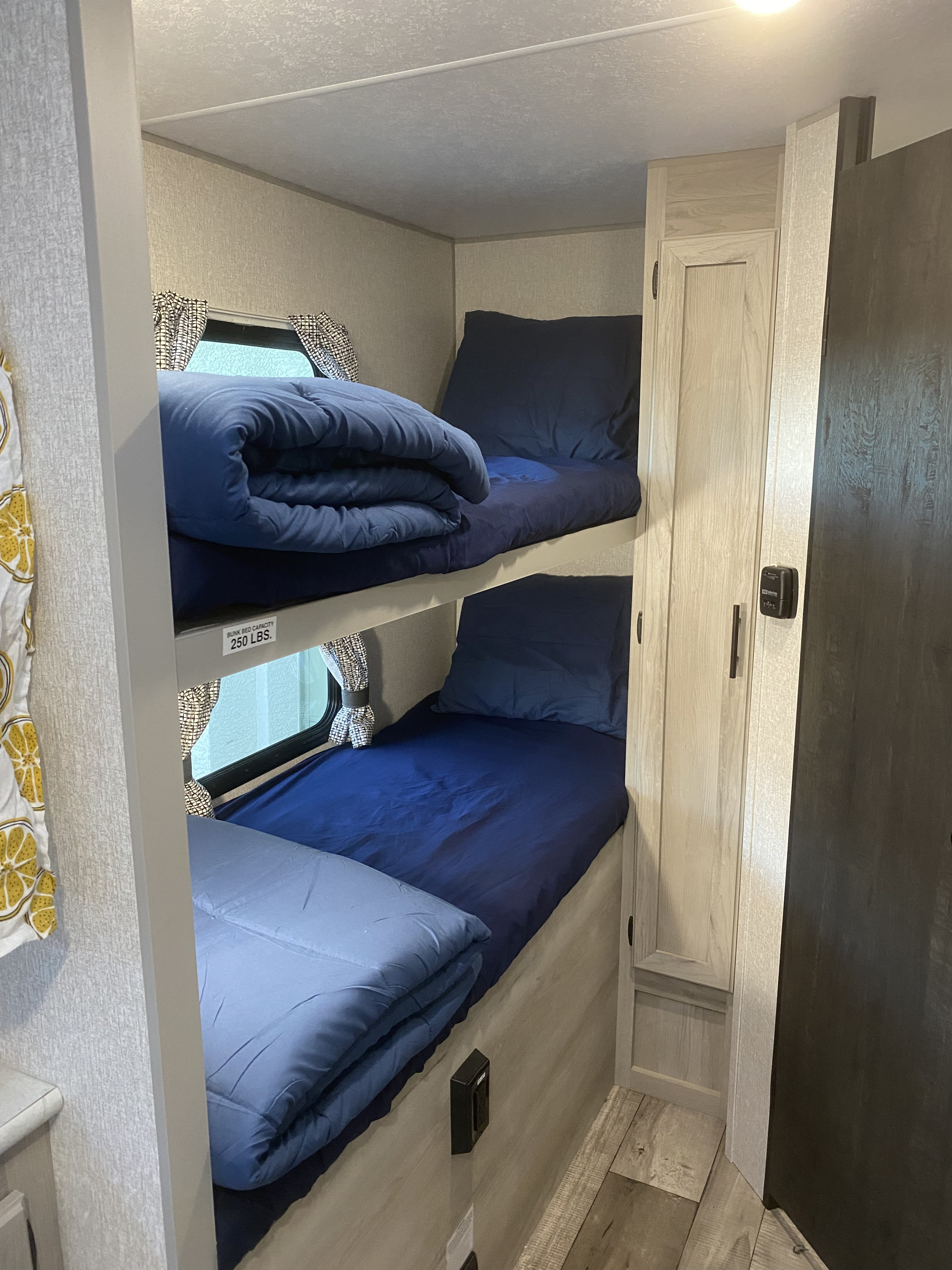 This rv rental offers practical bunk beds with blue bedding, side windows, and adjacent storage for family trips.. K-Z Manufacturing Sportsman Classic 2022
