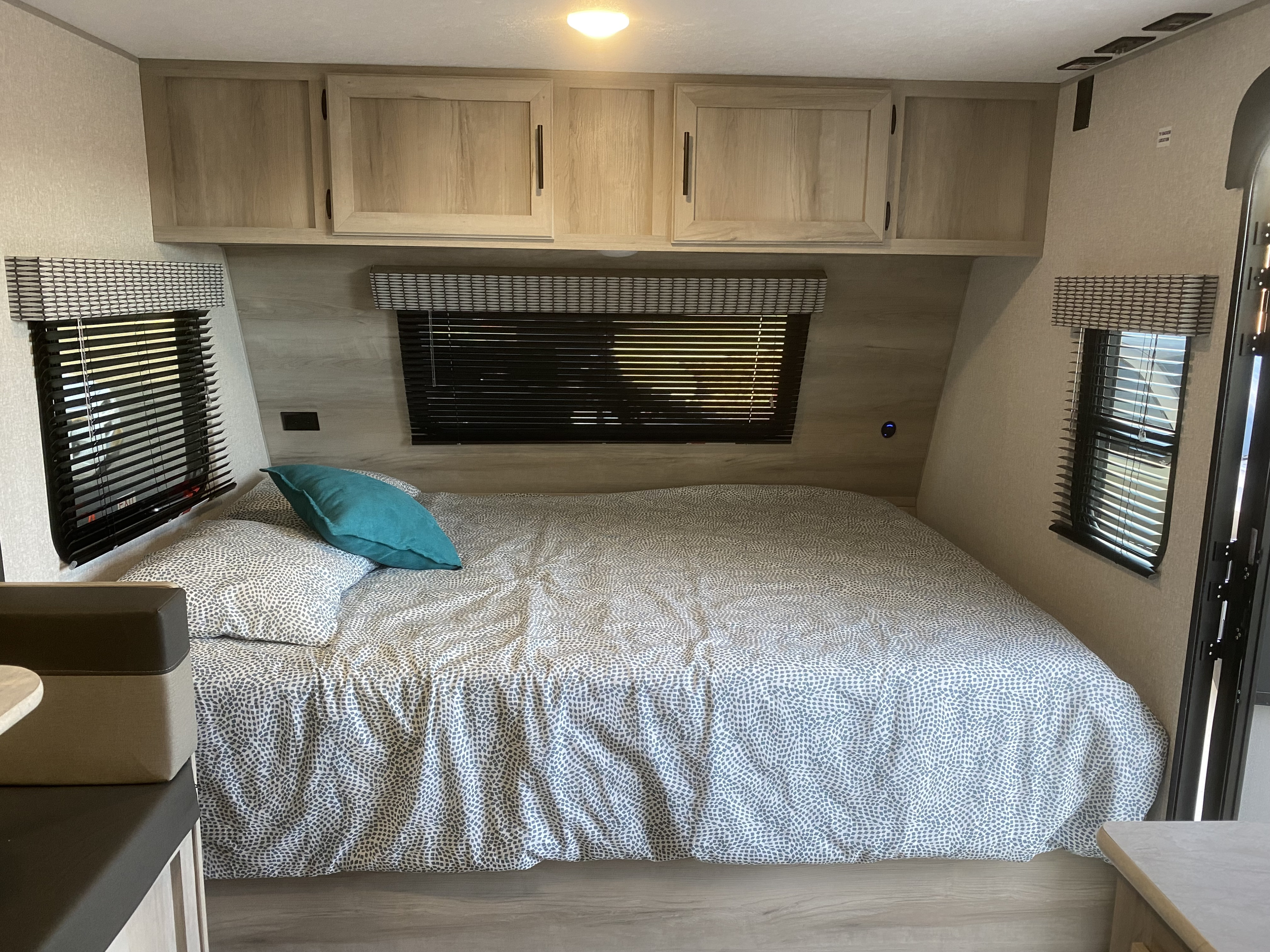 Inside a bright RV rental bedroom showing a bed with a patterned comforter, overhead cabinets, and large windows.. K-Z Manufacturing Sportsman Classic 2022