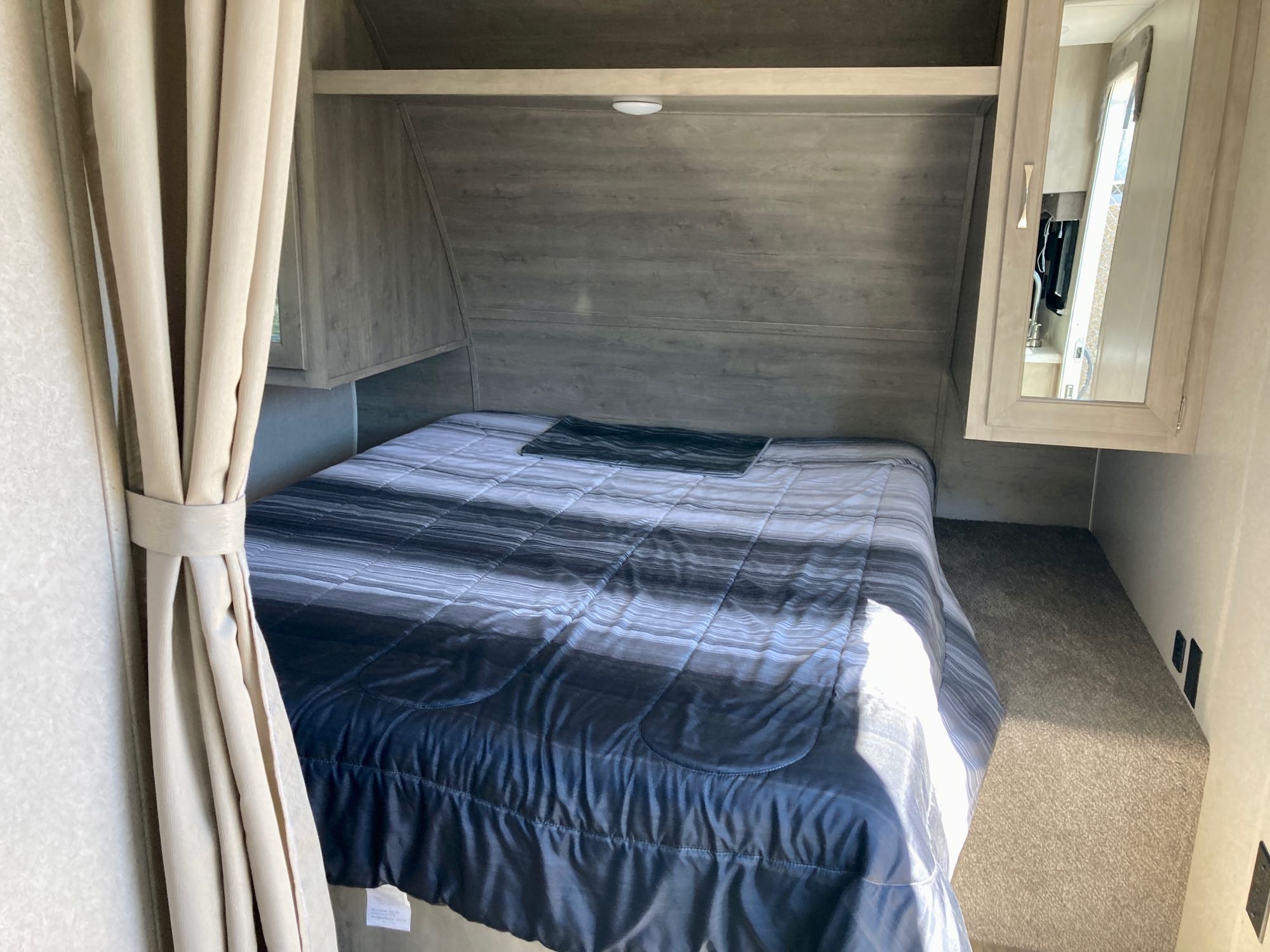 Inside an RV rental: a compact bedroom with a comfy bed, striped comforter, overhead storage, and a mirrored cabinet.. Palomino Puma XLE 20RLC 2019