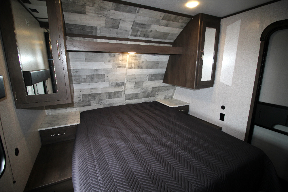 Compact RV rental bedroom with a comfy bed, overhead storage, and stylish wood-paneled wall for travel comfort.. Dutchmen Coleman 2022