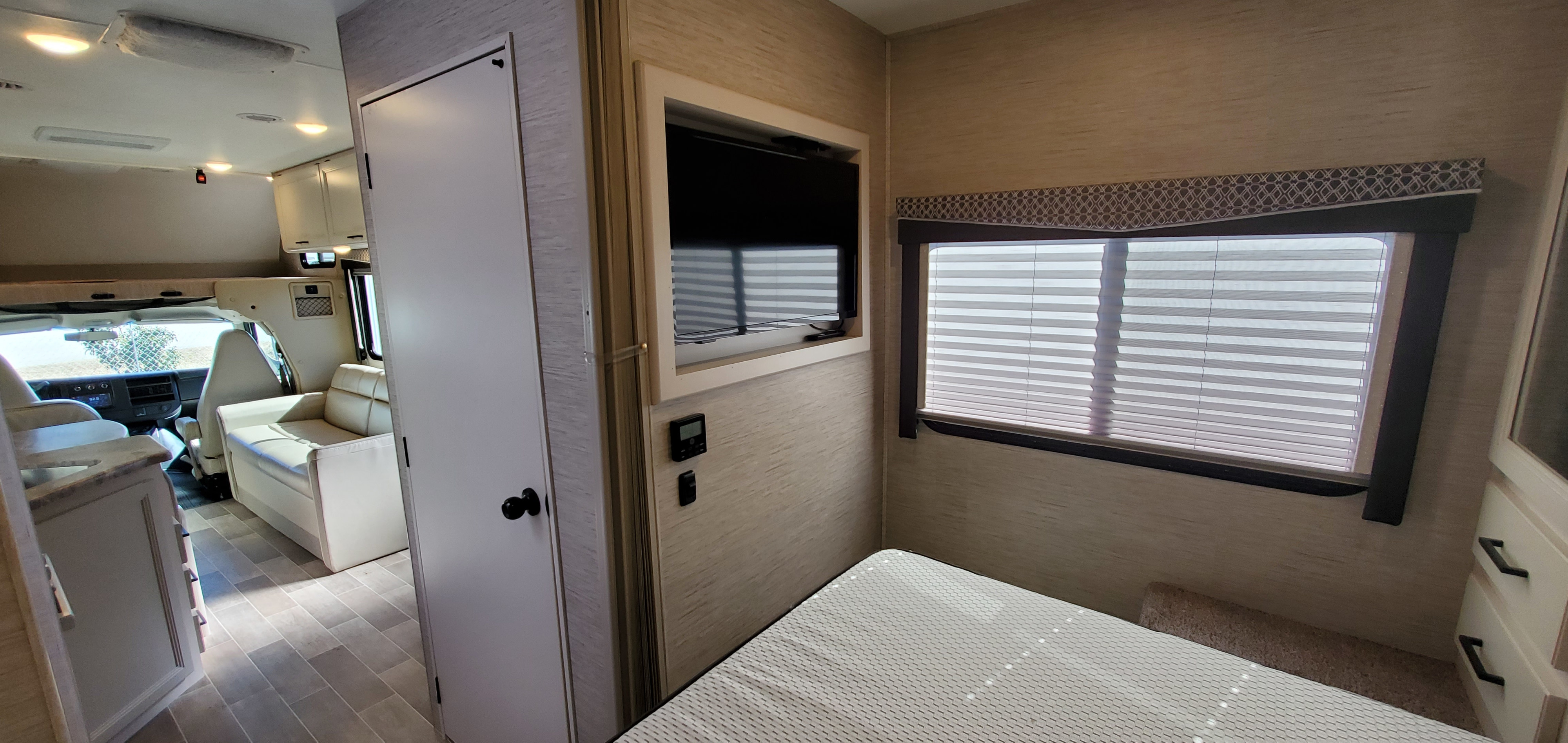 Bright RV rental interior. Features include a modern living space, driver's cabin, wall-mounted TV, and a cozy bedroom with bed.. Thor Motor Coach Chateau 2022