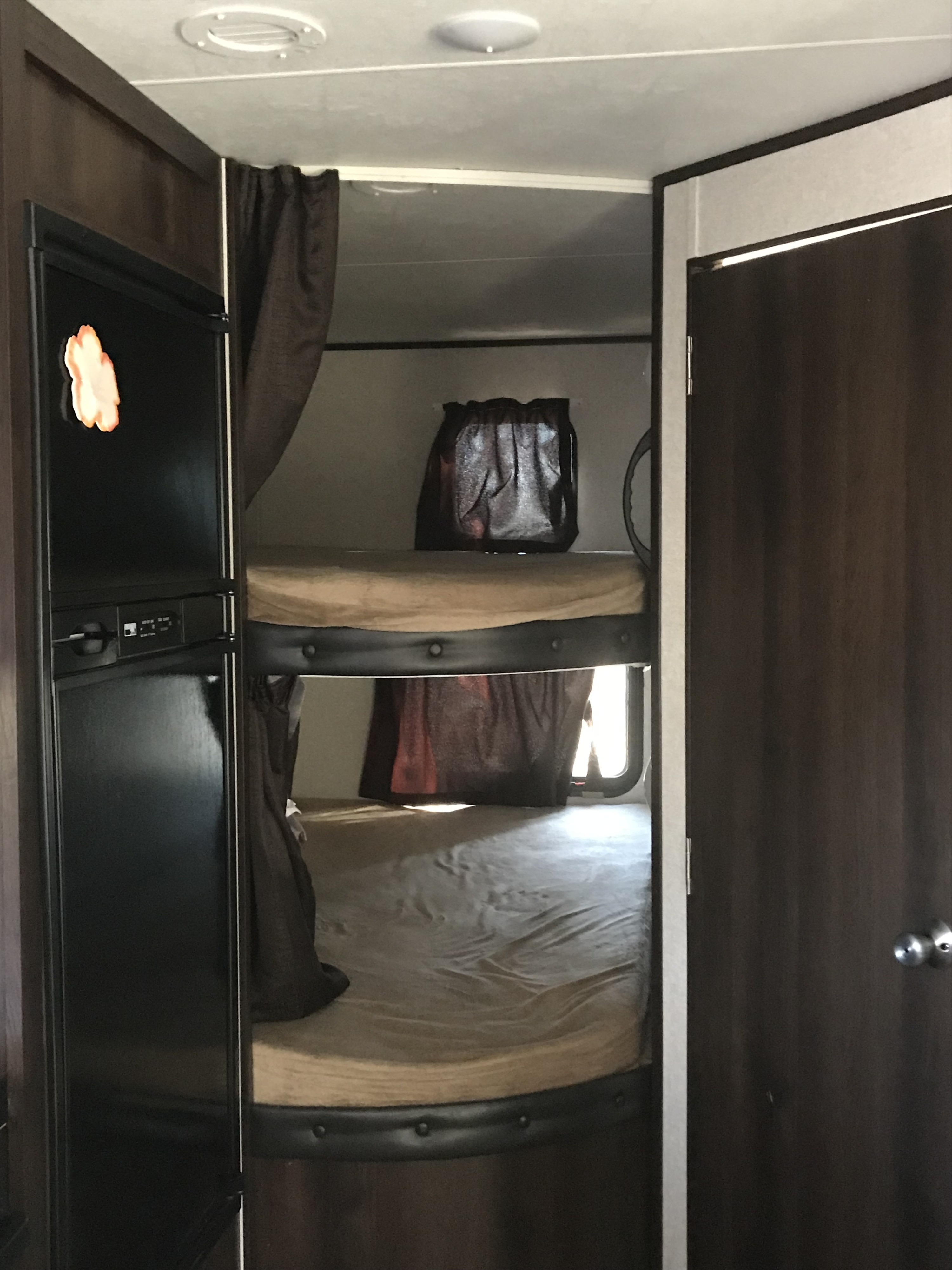 Inside an RV rental: a black refrigerator on the left and two comfortable bunk beds with dark frames and tan bedding.. Jayco Jay Flight 2018