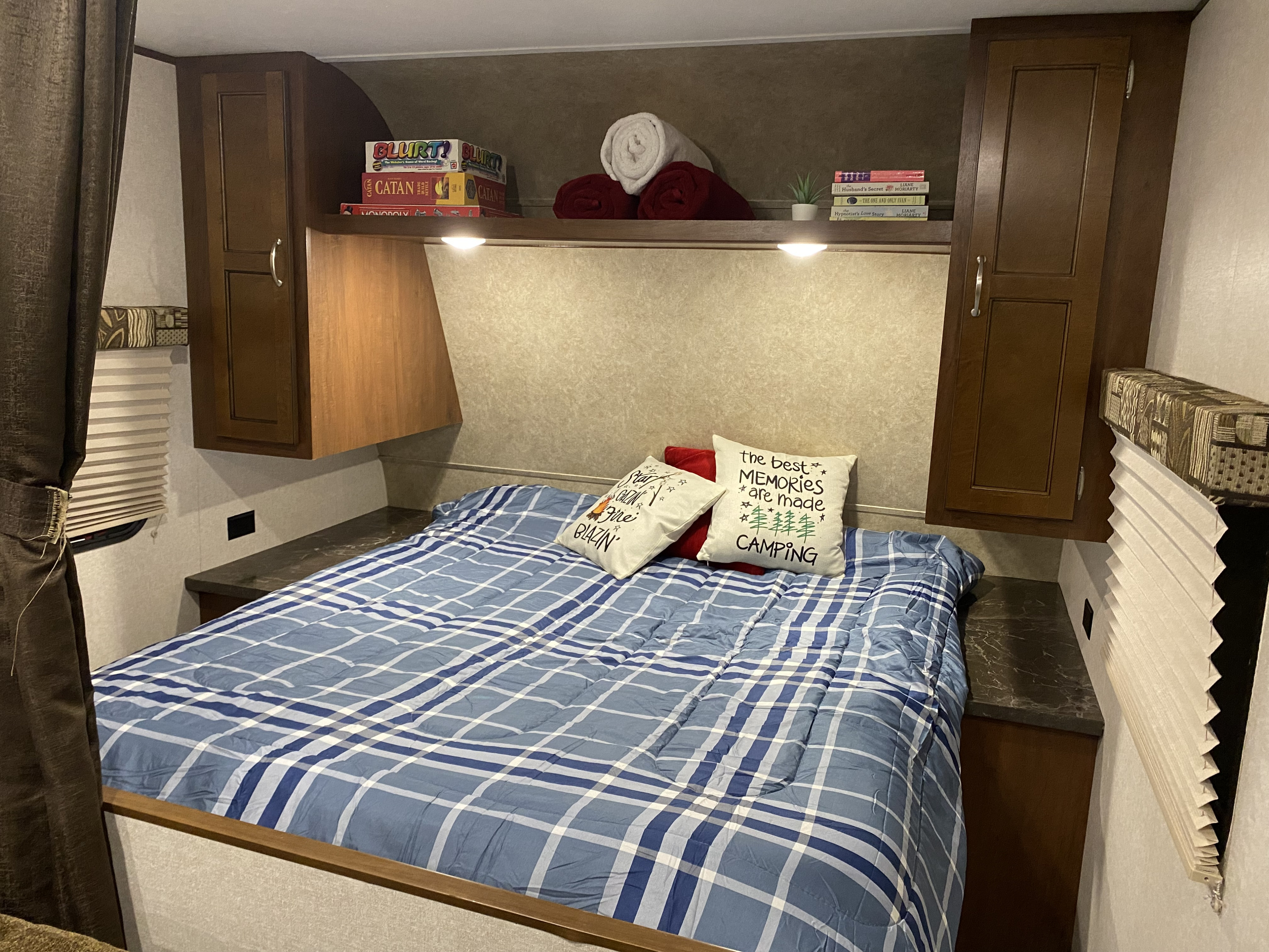 Cozy RV rental bedroom features plaid bedding, overhead cabinets with games, books, towels, and decorative pillows. Ideal for camping.. Jayco Jay Flight 2017