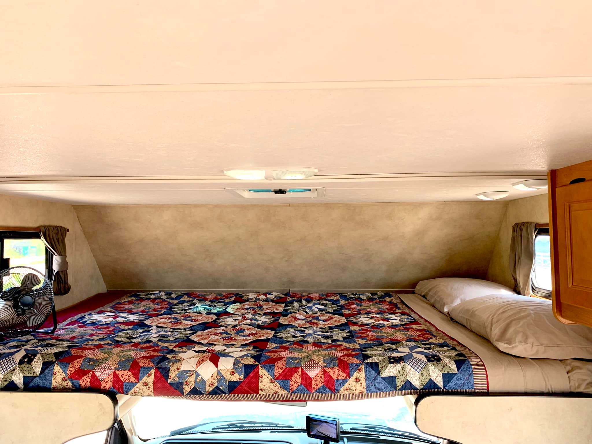 This RV rental offers a cozy sleeping area above the cab, featuring a colorful patchwork quilt, fan, and pillows.. Thor Motor Coach Four Winds Majestic 2016