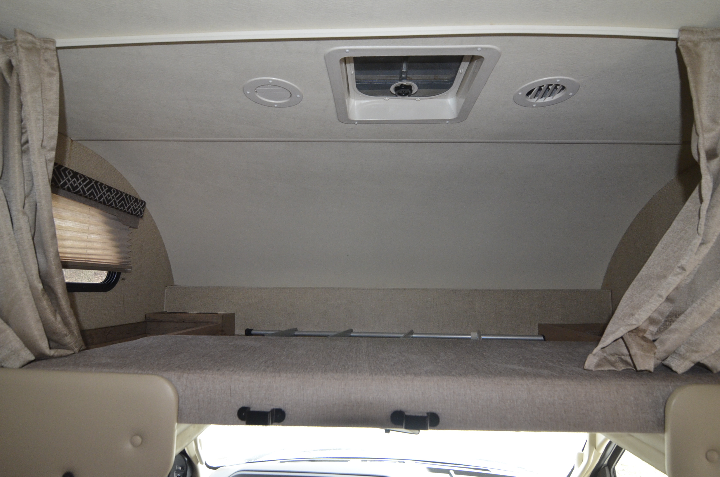 Interior of an RV rental: a spacious over-cab bunk bed with safety rail, window, vents, and side curtains.. Four Winds 28Z 2018