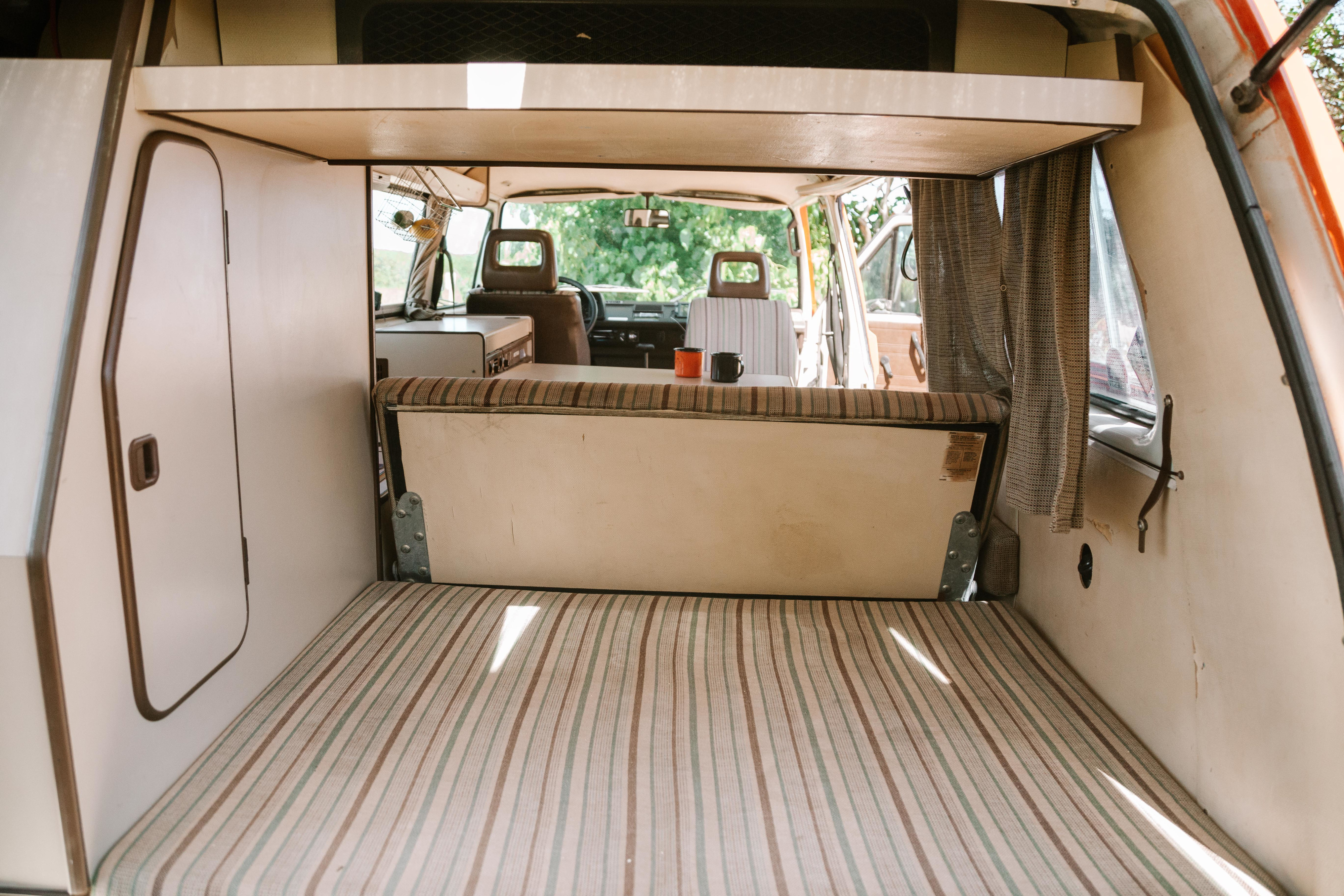 Cozy camper van interior for your RV rental. View from rear shows striped bed, seating, and front cabin area with mugs.. Volkswagen Westfalia 1983