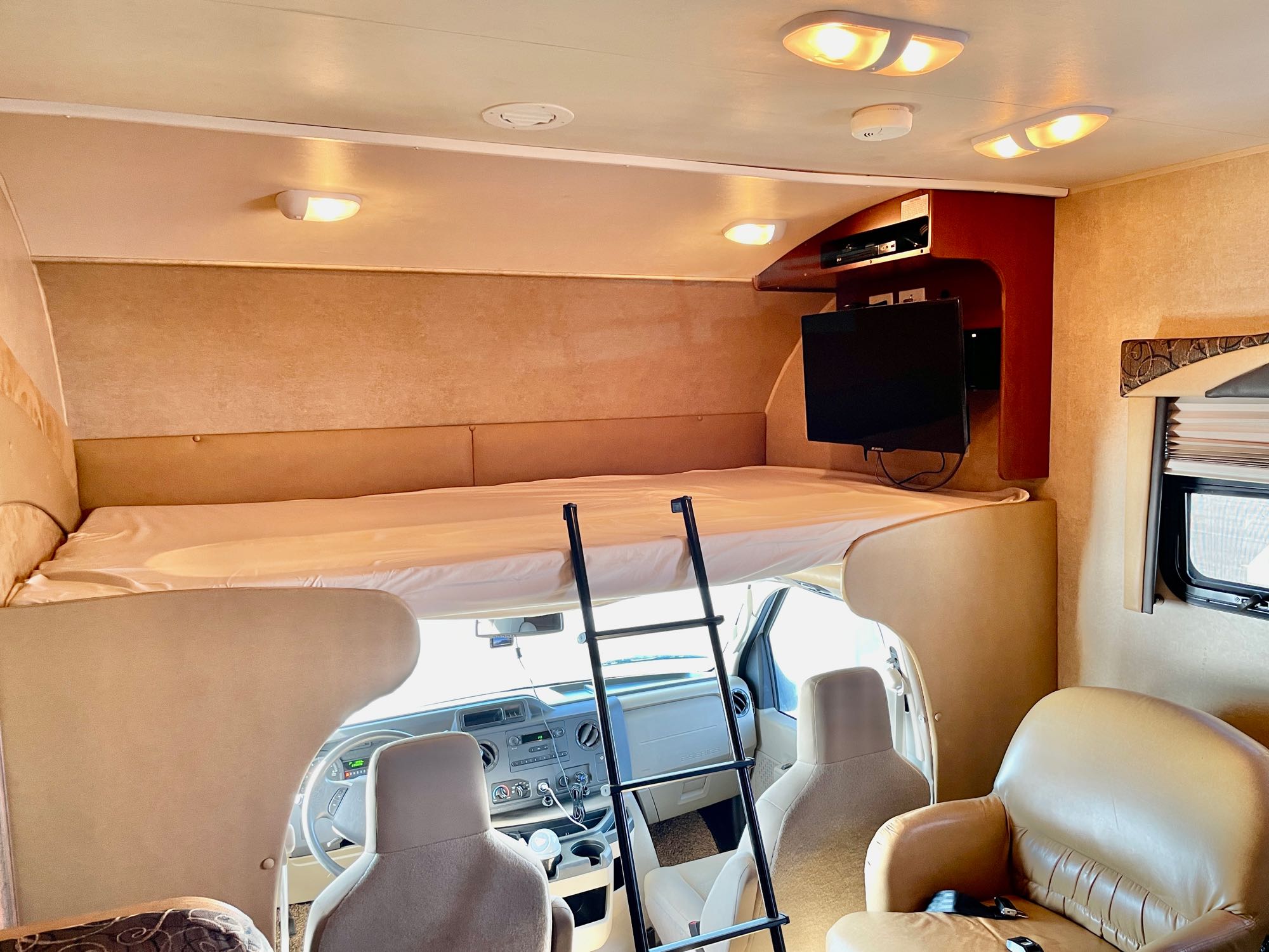 RV rental interior showing a cozy overhead bunk bed with a ladder, driver's area below, and living space.. Jayco Redhawk 2014