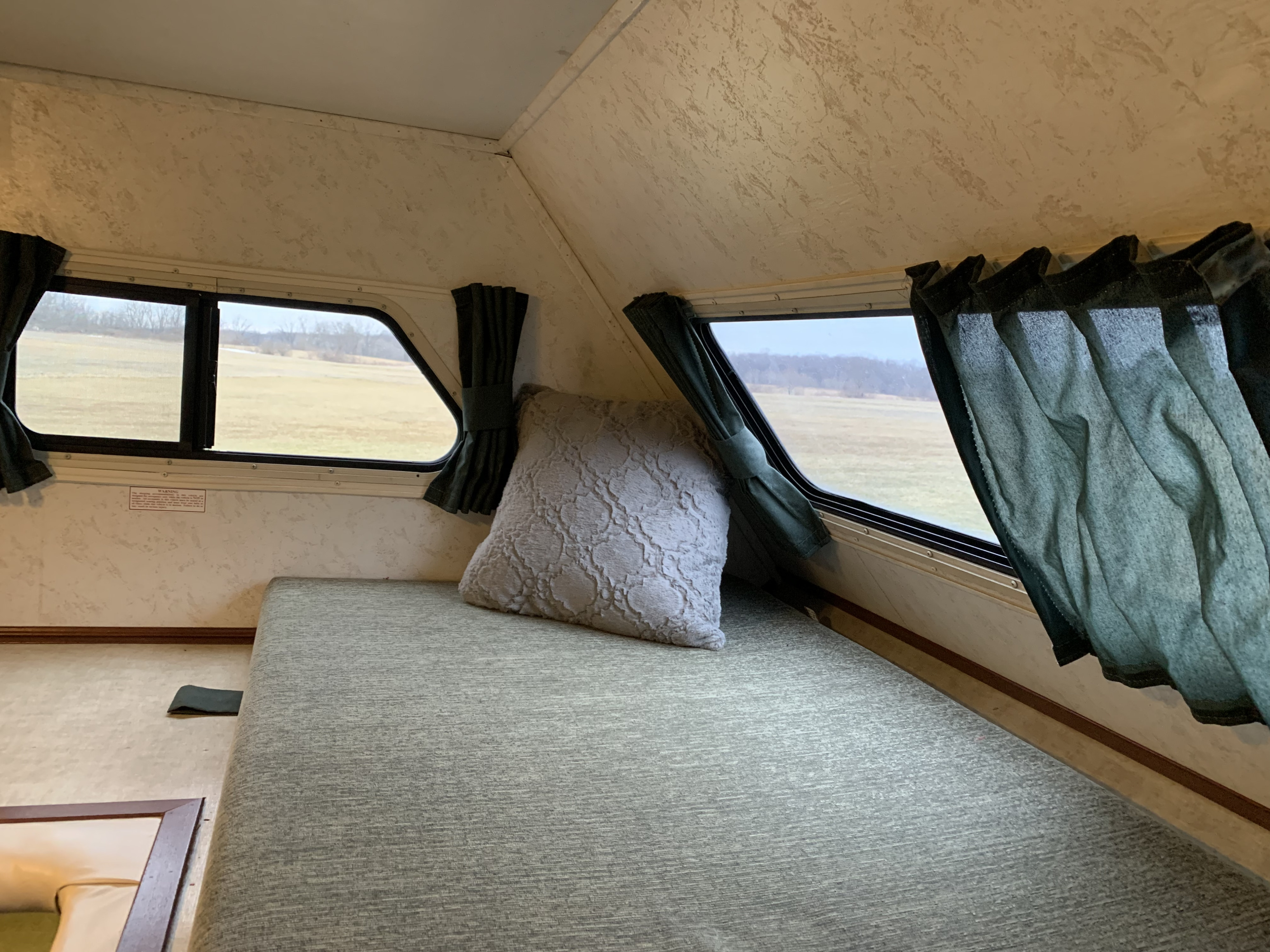 Cozy RV rental interior with a comfy bed, windows revealing a wide-open field view.. Thor Motor Coach Chateau 2001