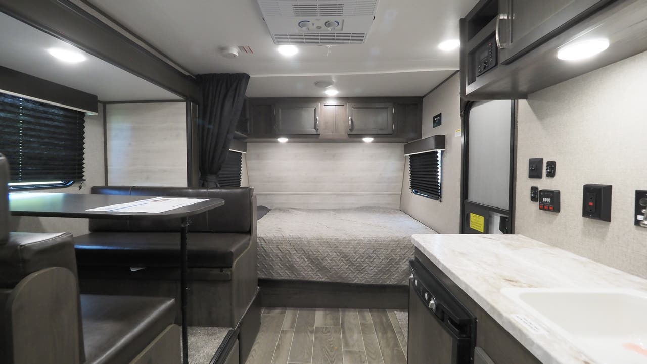 This RV rental interior features a cozy bed, dinette, and compact kitchen area, ideal for travel adventures.. Jayco 184BS 2022