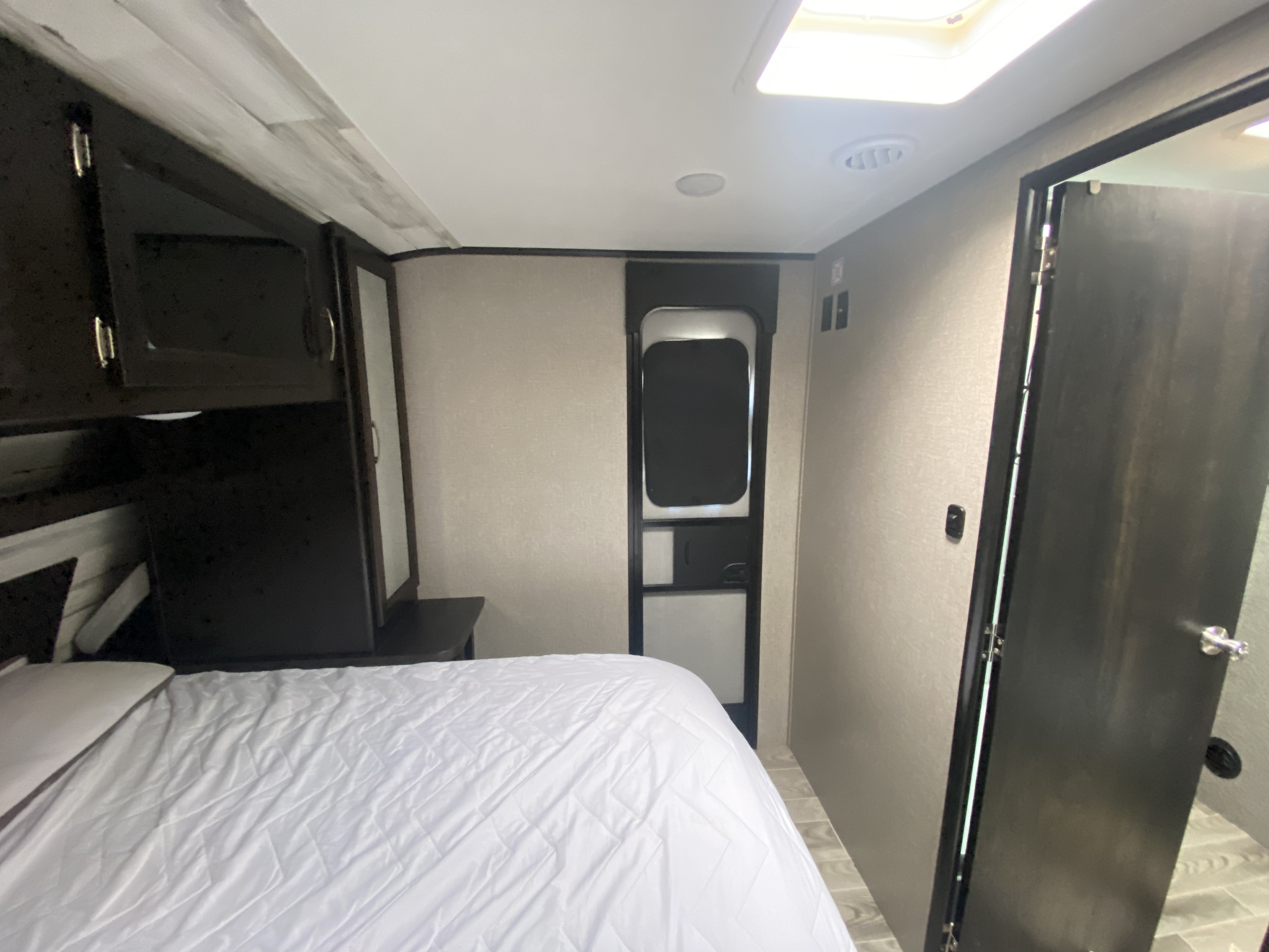 Cozy RV rental bedroom showcasing a compact design, comfortable bed, overhead cabinets, and interior doors.. Jayco Jay Feather 2021