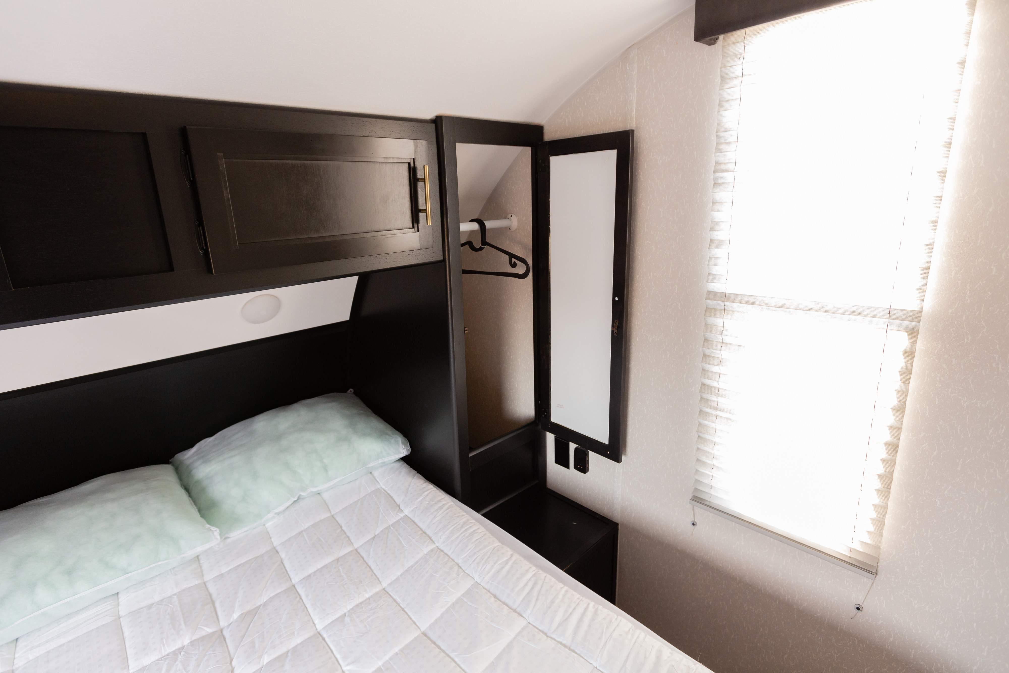 RV rental interior: cozy bedroom with dark wood cabinets, a comfortable bed, and a wardrobe. Bright window illuminates the space.. Forest River Cherokee Grey Wolf 2021