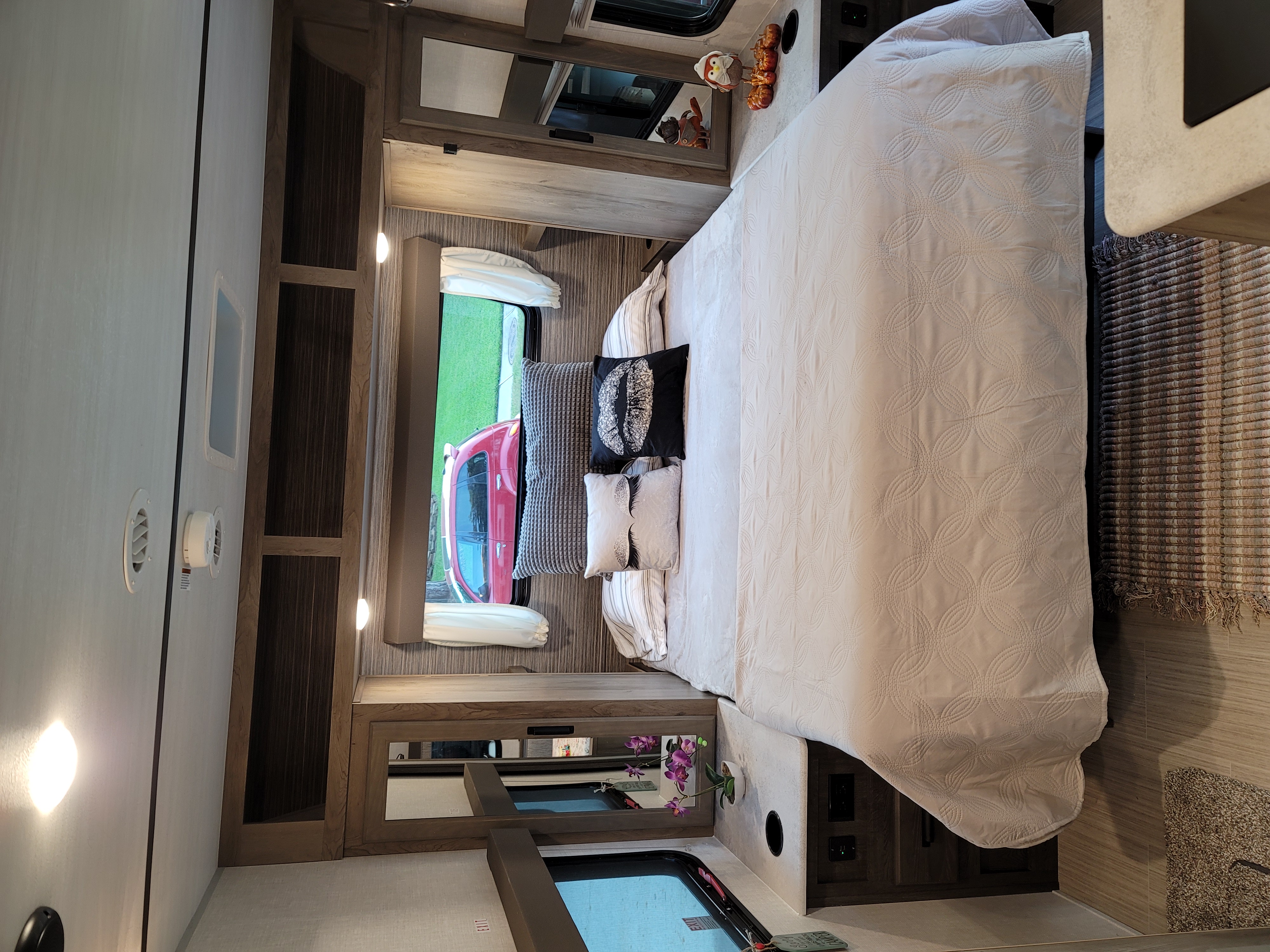 Cozy RV rental bedroom featuring a large bed with a quilted spread, decorative pillows, and window views of a red car outside.. Forest River Surveyor 2021
